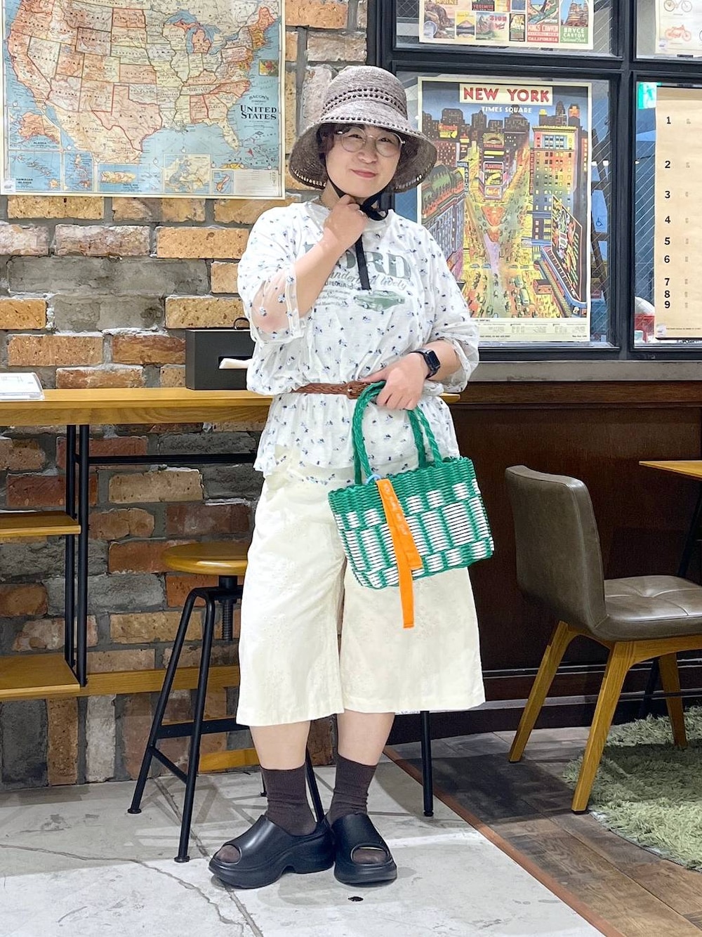 ブラック系のサンダル、ベージュ系のTシャツ/カットソー、グリーン系のかごバッグを着用したレディースの夏コーディネートの1枚目の写真