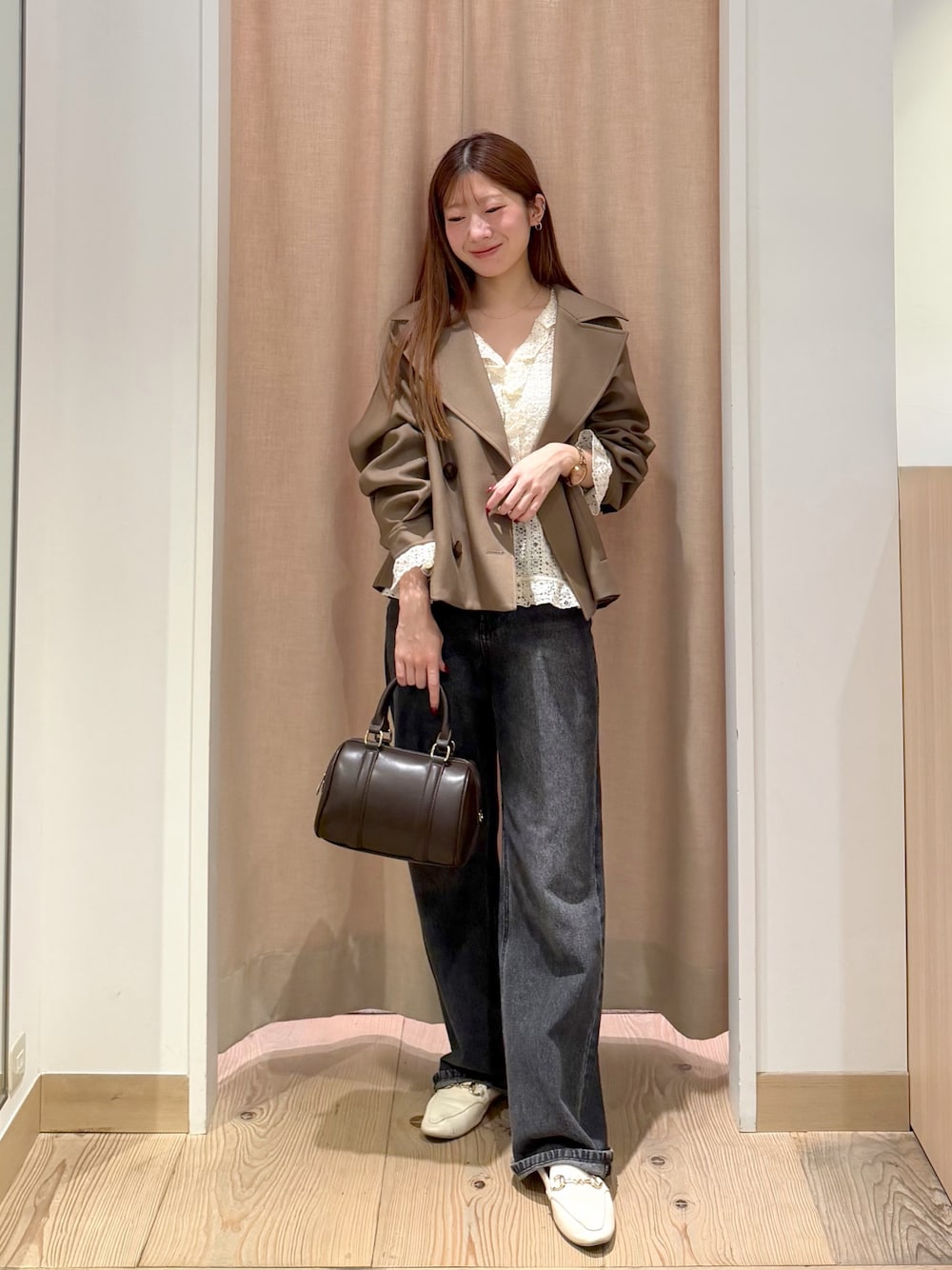 ブラック系のデニムパンツ、ブラウン系のボストンバッグ、ブラウン系のトレンチコートを着用したレディースの秋コーディネートの1枚目の写真