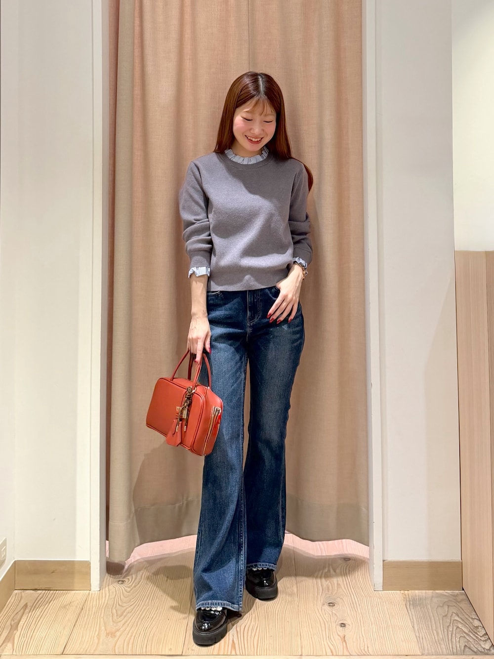 オレンジ系のボストンバッグ、ブルー系のデニムパンツ、グレー系のニット/セーターを着用したレディースの秋コーディネートの1枚目の写真