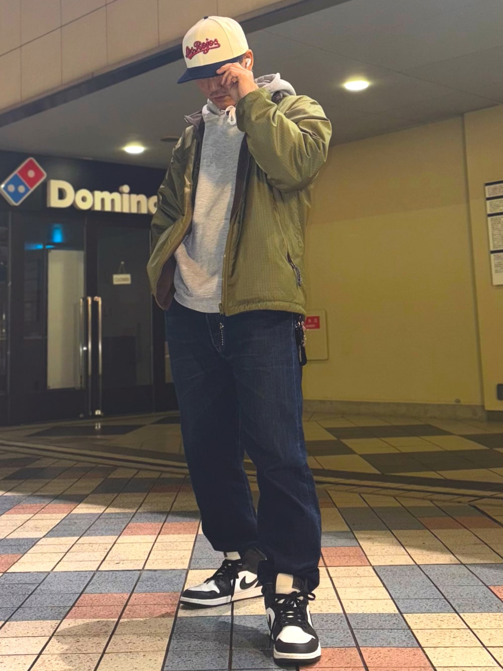 グリーン系のナイロンジャケット、グレー系のパーカー、ブルー系のデニムパンツを着用したメンズの冬コーディネートの1枚目の写真