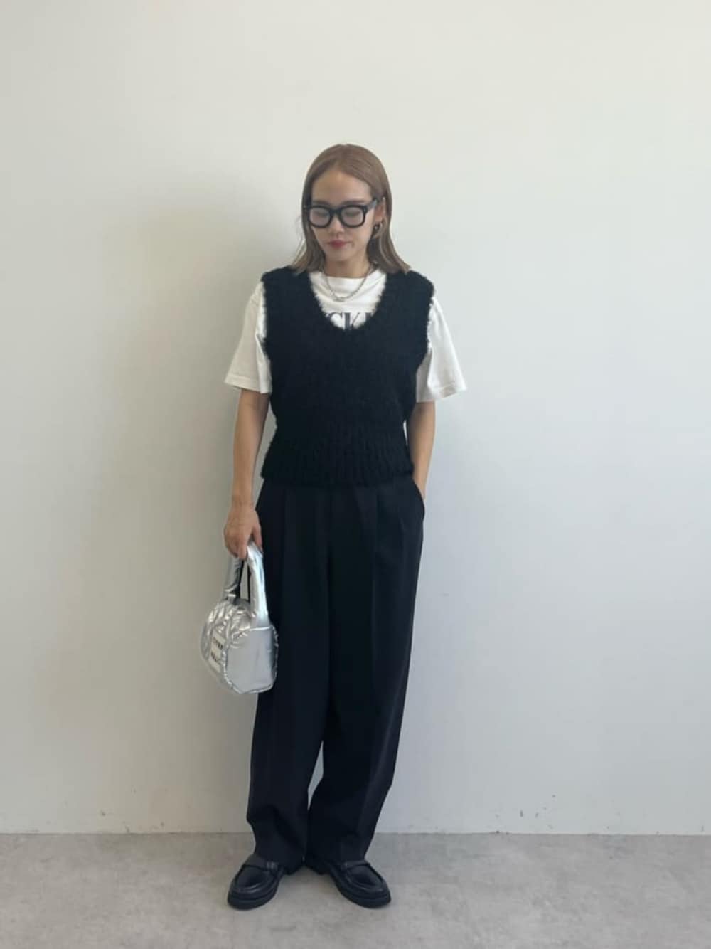 シルバー系のハンドバッグ、ブラック系のローファー、ブラック系のスラックスを着用したレディースの秋コーディネートの1枚目の写真