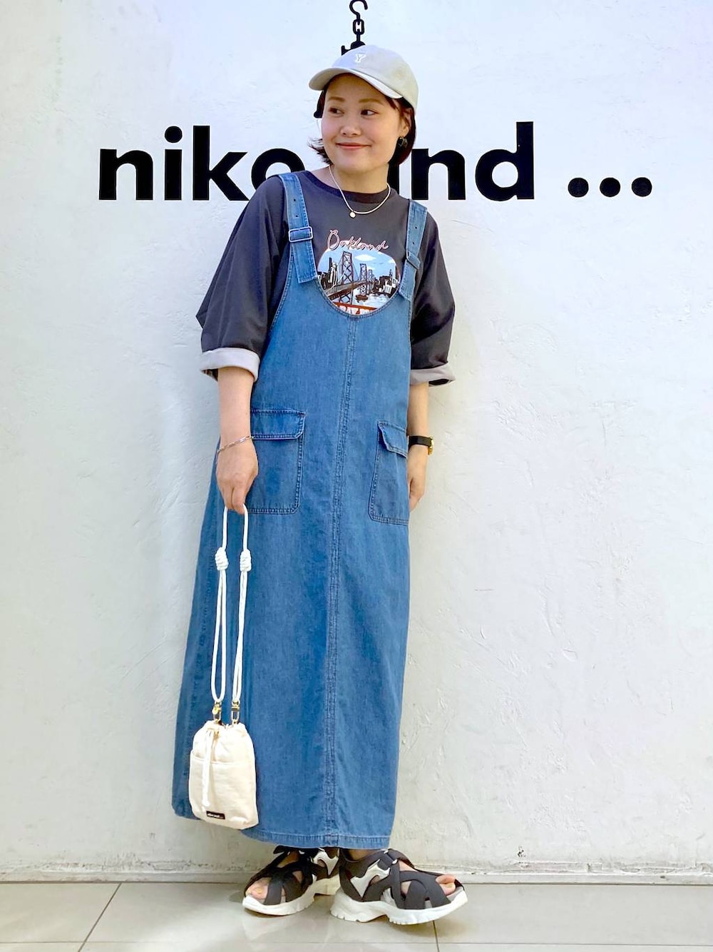 ホワイト系のショルダーバッグ、グレー系のTシャツ/カットソー、ブルー系のジャンパースカートを着用したレディースの夏コーディネートの1枚目の写真