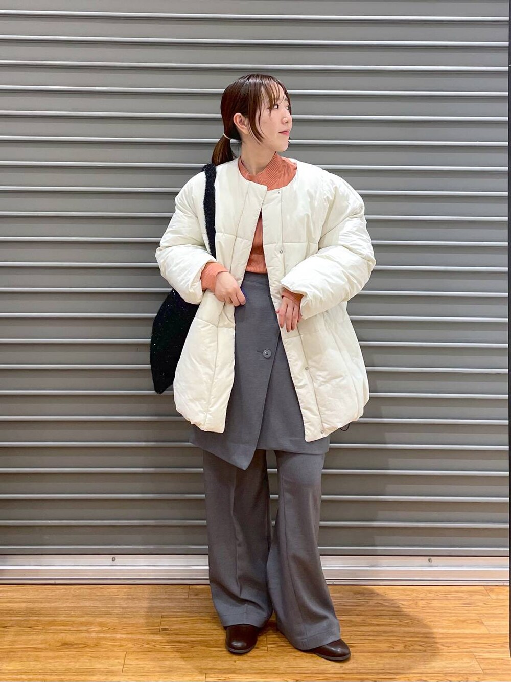 オレンジ系のニット/セーター、ブラウン系のブーツ、ブラック系のショルダーバッグを着用したレディースの冬コーディネートの1枚目の写真