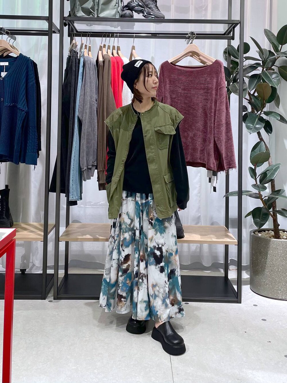 グリーン系のベスト、ブラック系のTシャツ/カットソー、ブルー系のスカートを着用したレディースの秋コーディネートの1枚目の写真