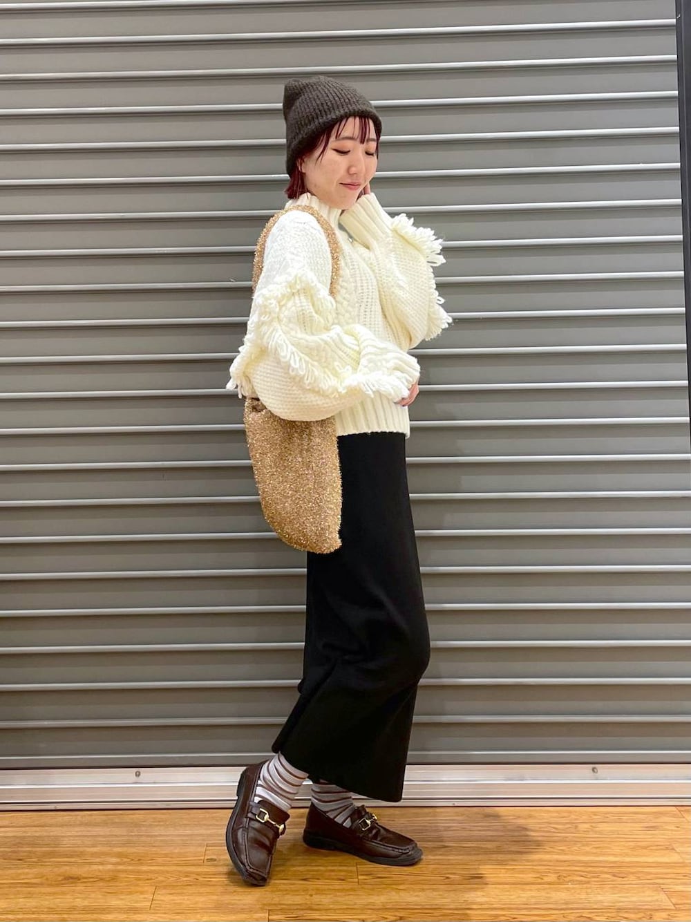 ブラック系のスカート、ゴールド系のショルダーバッグ、ホワイト系のニット/セーターを着用したレディースの冬コーディネートの1枚目の写真