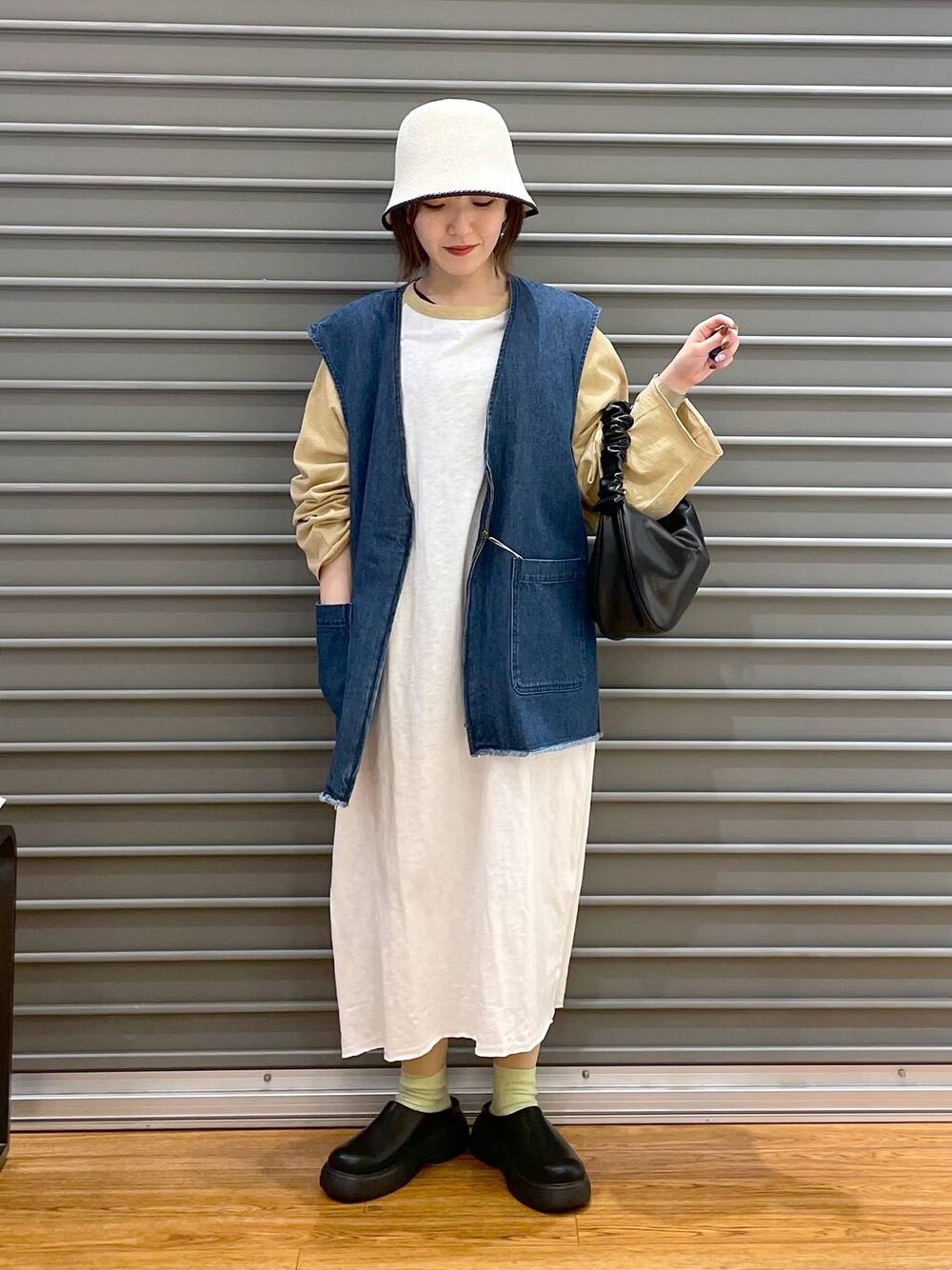 ベージュ系のワンピース、ブラック系のショルダーバッグ、ブルー系のベストを着用したレディースの春コーディネートの1枚目の写真