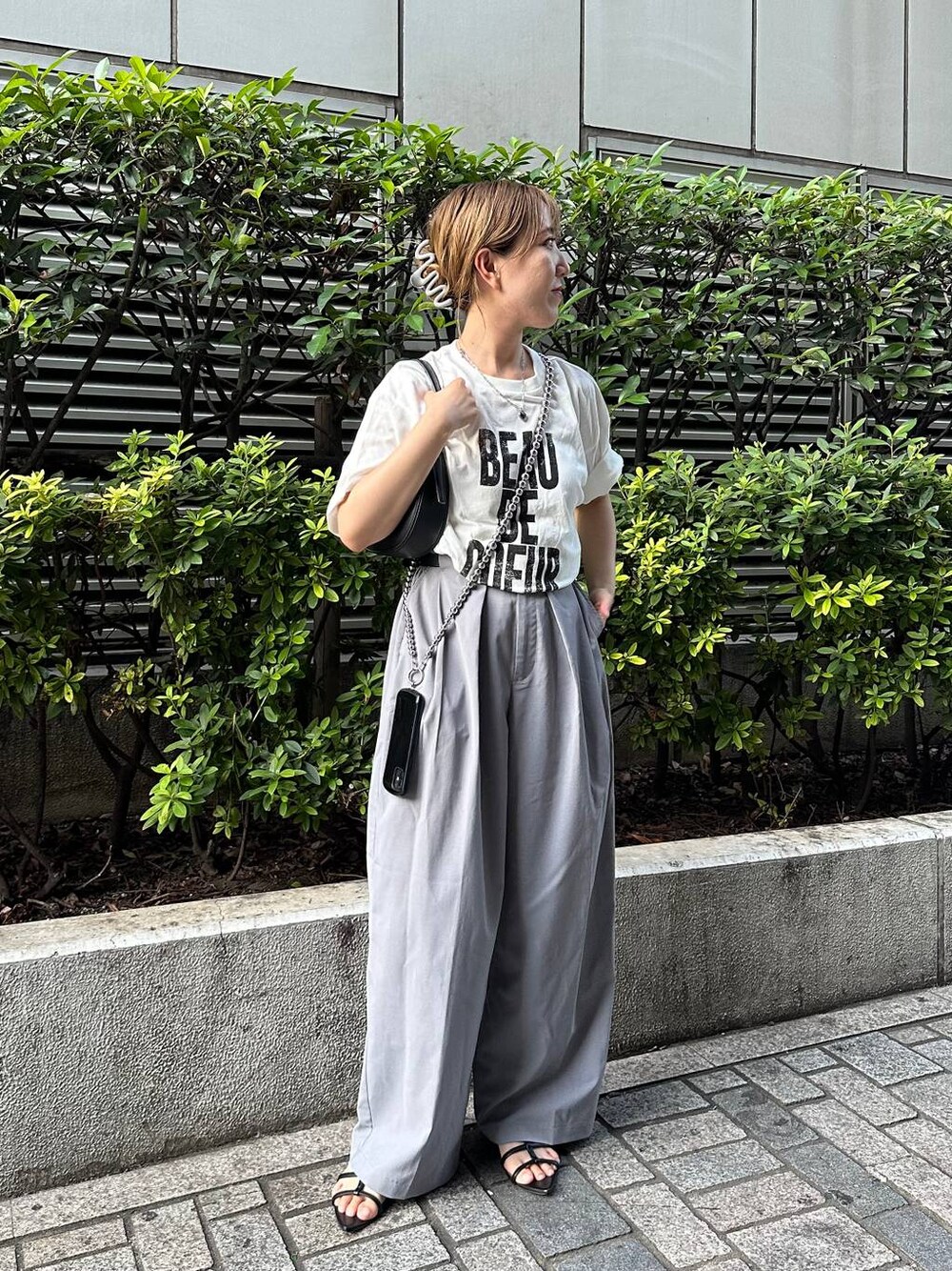 グレー系のスラックス、ホワイト系のTシャツ/カットソー、シルバー系のスマホグッズを着用したレディースの夏コーディネートの1枚目の写真