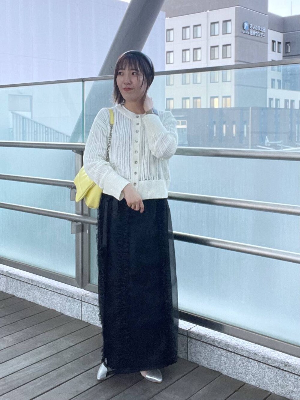 イエロー系のショルダーバッグ、ブラック系のスカート、グレー系のパンプスを着用したレディースの夏コーディネートの1枚目の写真