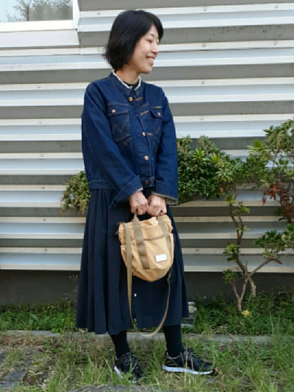 ベージュ系のショルダーバッグ、ブルー系のデニムジャケット、ブラック系のスニーカーを着用したレディースの秋コーディネートの1枚目の写真