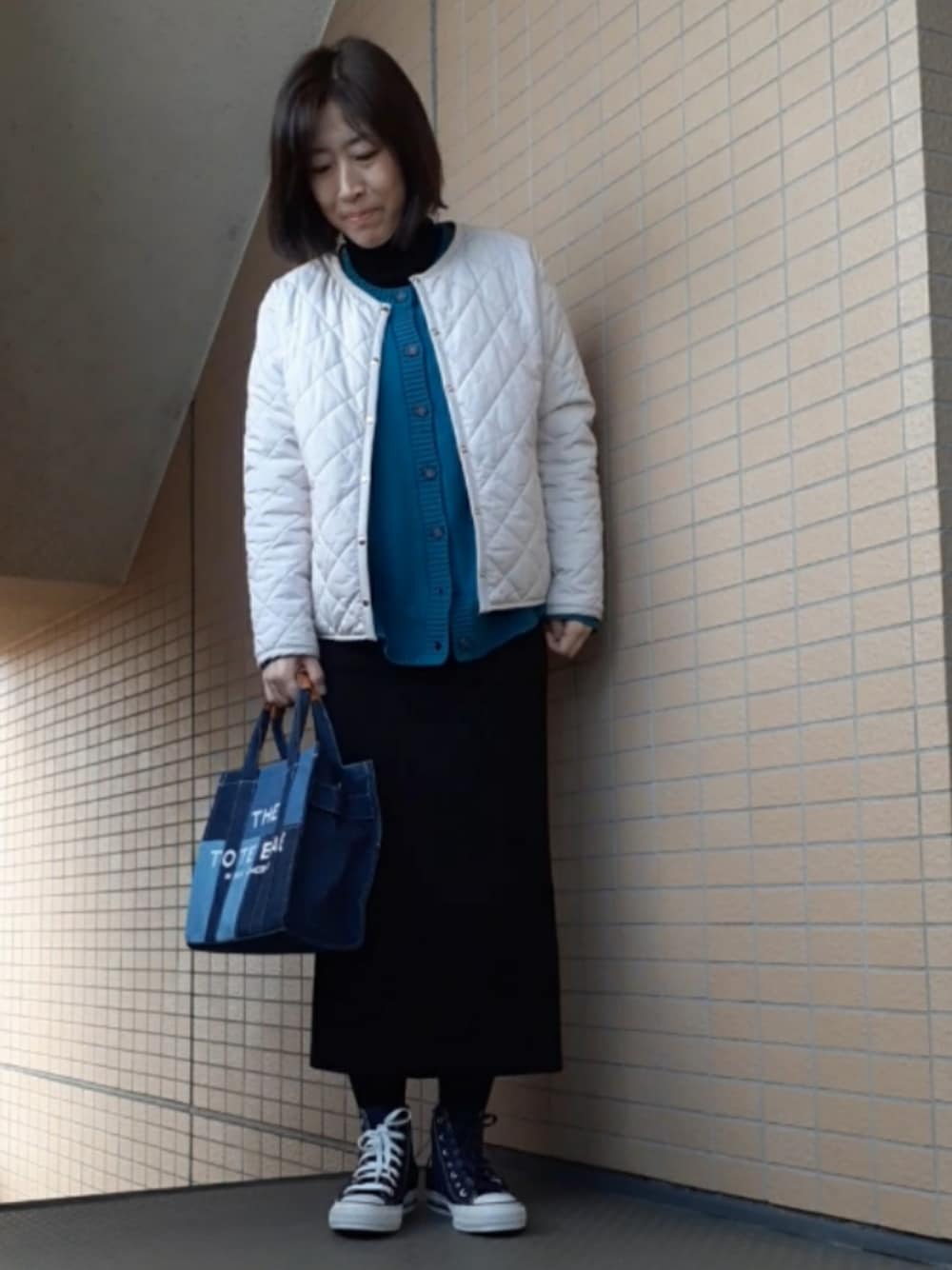 ブルー系のスニーカー、ブラック系のスカート、ホワイト系のノーカラージャケットを着用したレディースの冬コーディネートの1枚目の写真