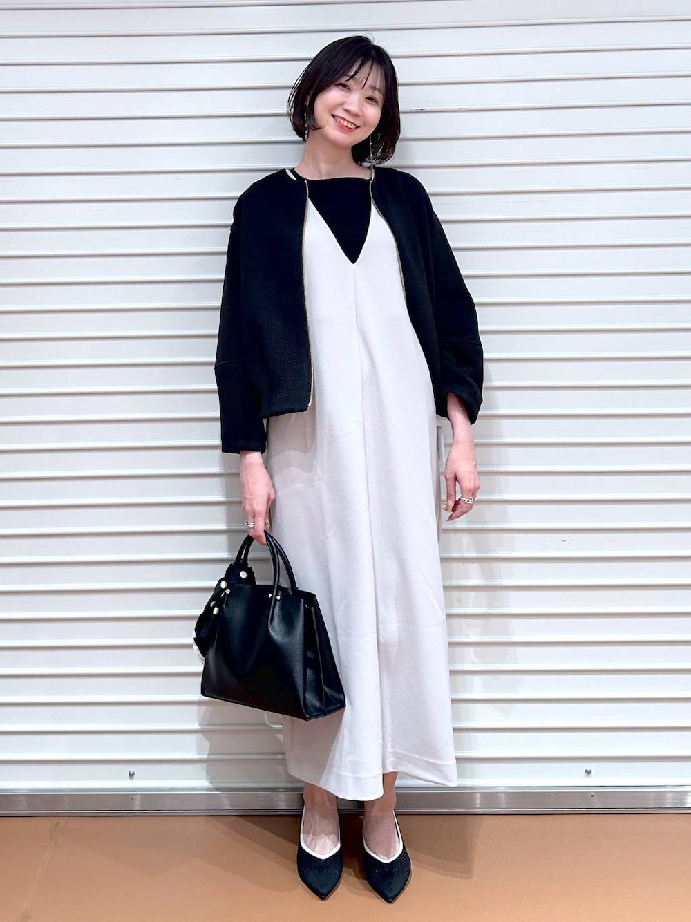 ブラック系のパンプス、ブラック系のショルダーバッグ、ベージュ系のジャンパースカートを着用したレディースの春コーディネートの1枚目の写真