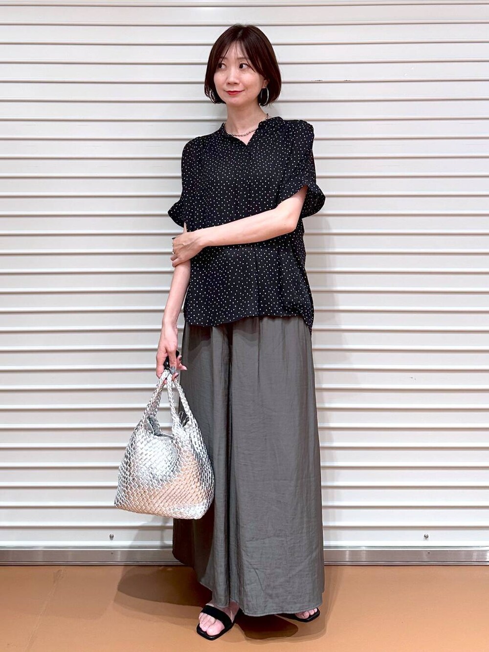 シルバー系のトートバッグ、ブラック系のサンダル、ブラック系のシャツ/ブラウスを着用したレディースの夏コーディネートの1枚目の写真