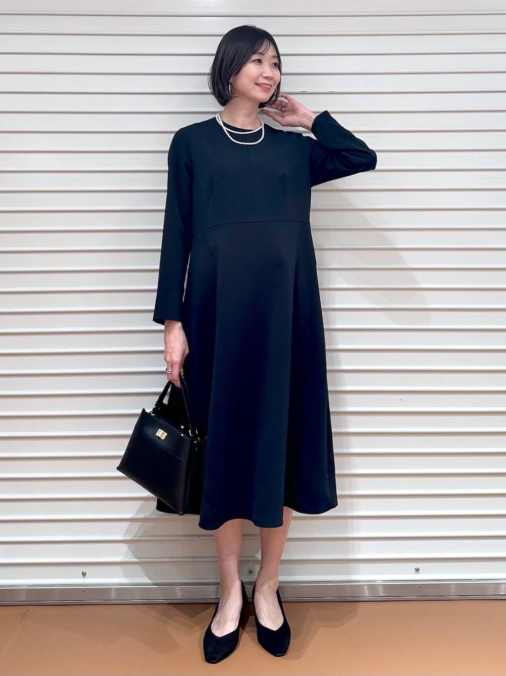 ブルー系のワンピース、ブラック系のハンドバッグ、ブラック系のパンプスを着用したレディースの春コーディネートの1枚目の写真