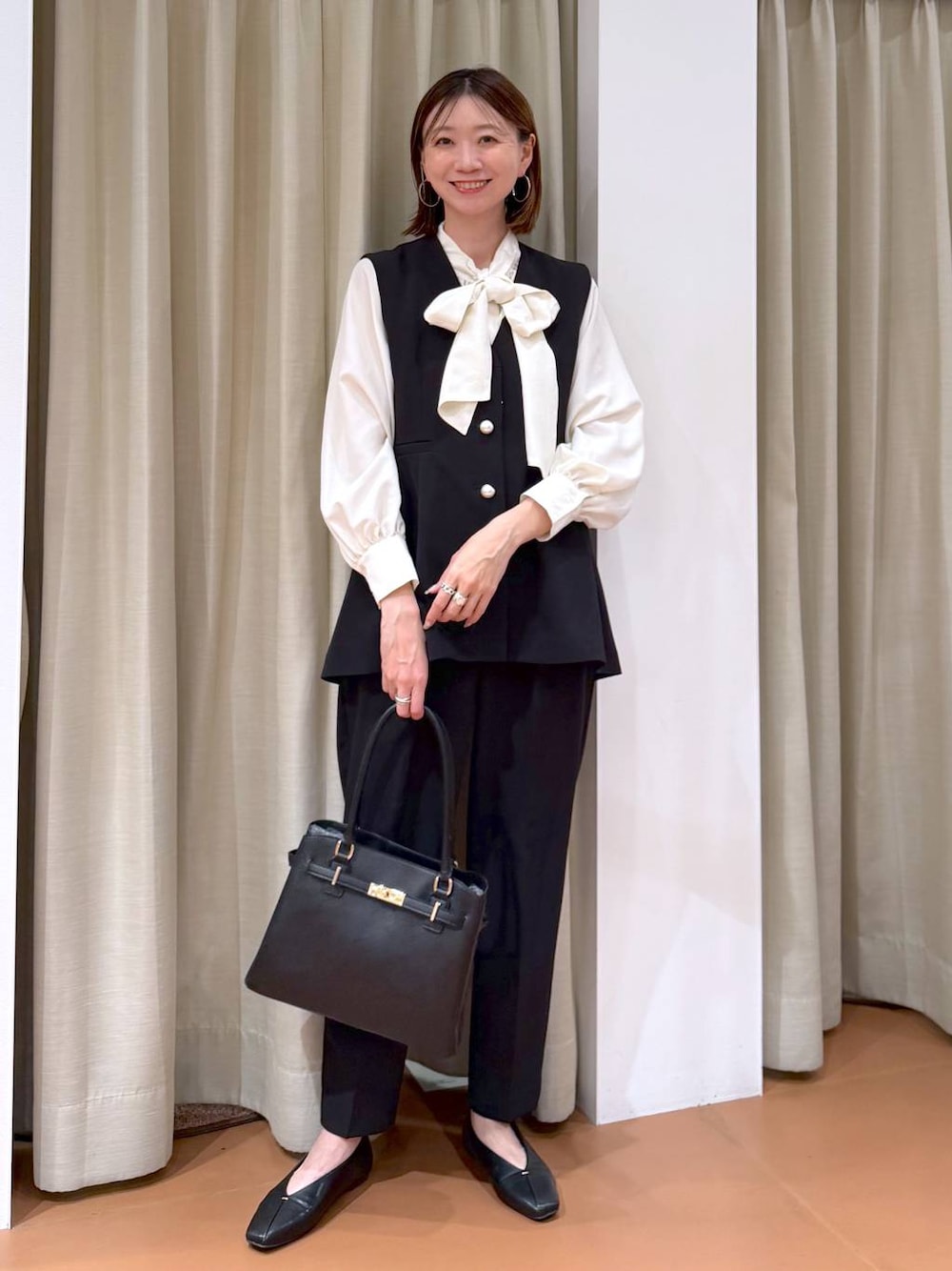 ブラック系のパンプス、ブラック系のスラックス、ブラック系のベストを着用したレディースの冬コーディネートの1枚目の写真