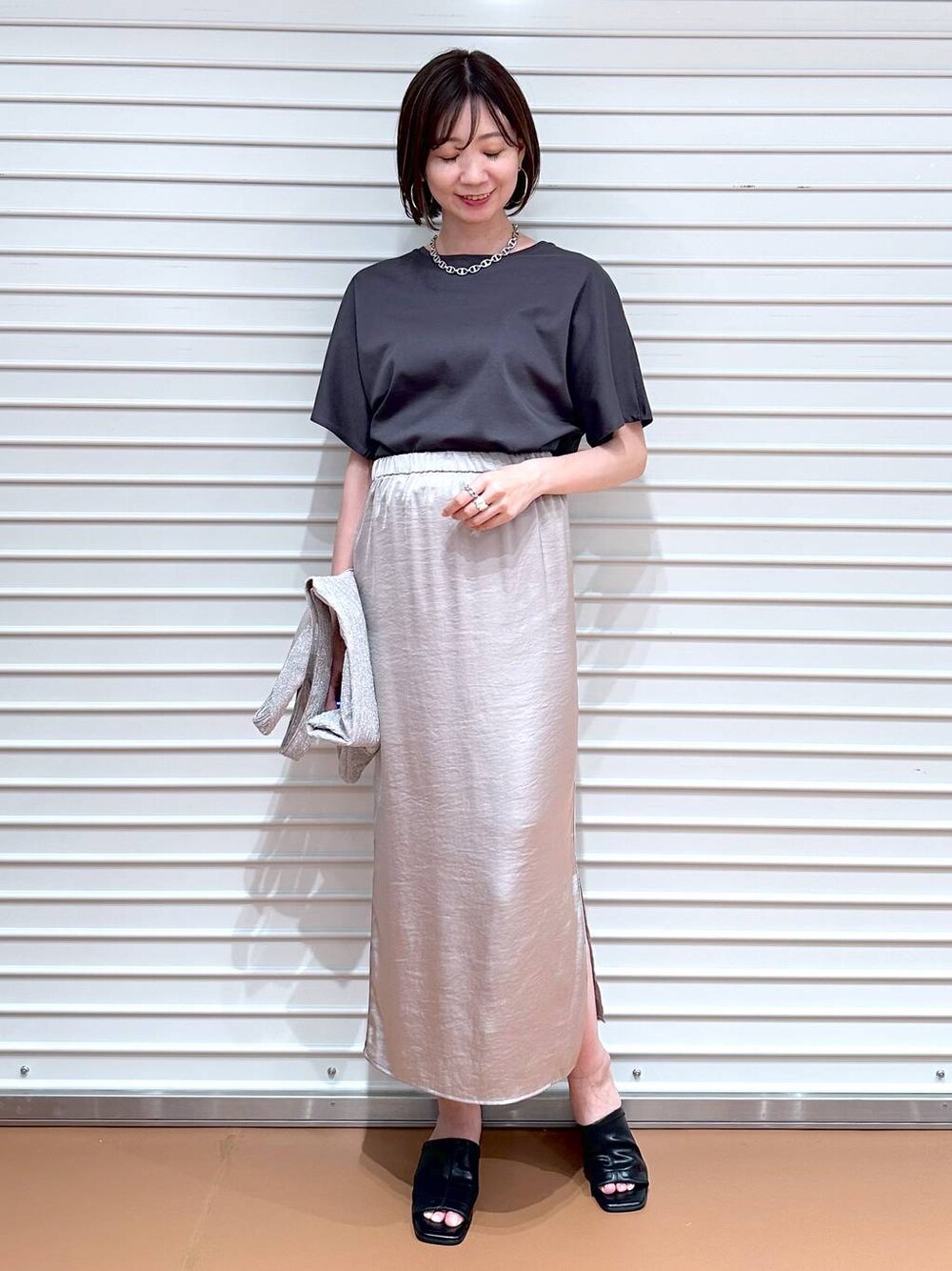 ベージュ系のスカート、ブラック系のサンダル、グレー系のTシャツ/カットソーを着用したレディースの春コーディネートの1枚目の写真