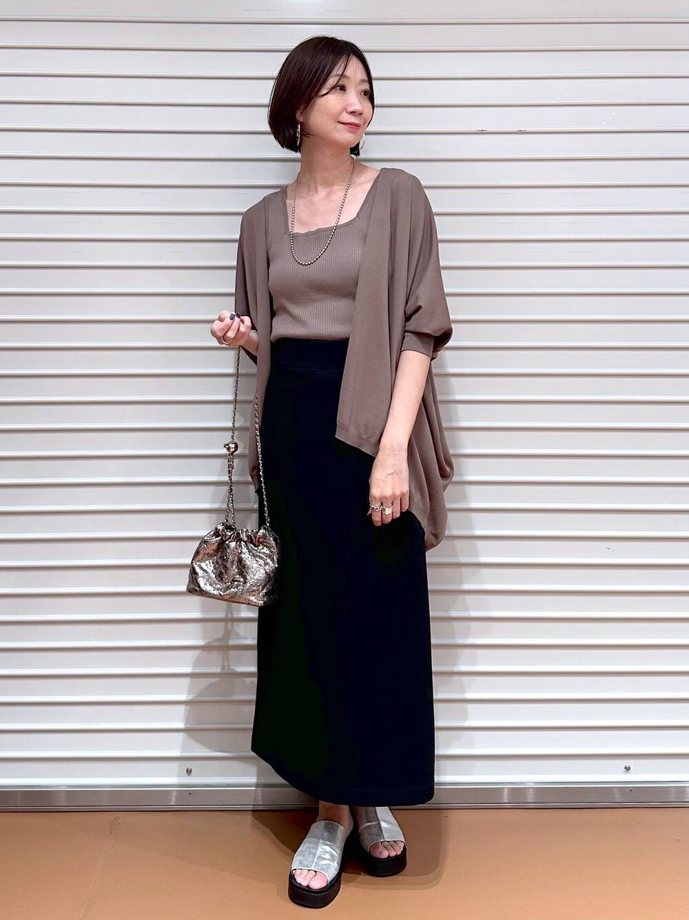 ブラック系のスカート、ブラウン系のカーディガン/ボレロ、シルバー系のサンダルを着用したレディースの夏コーディネートの1枚目の写真