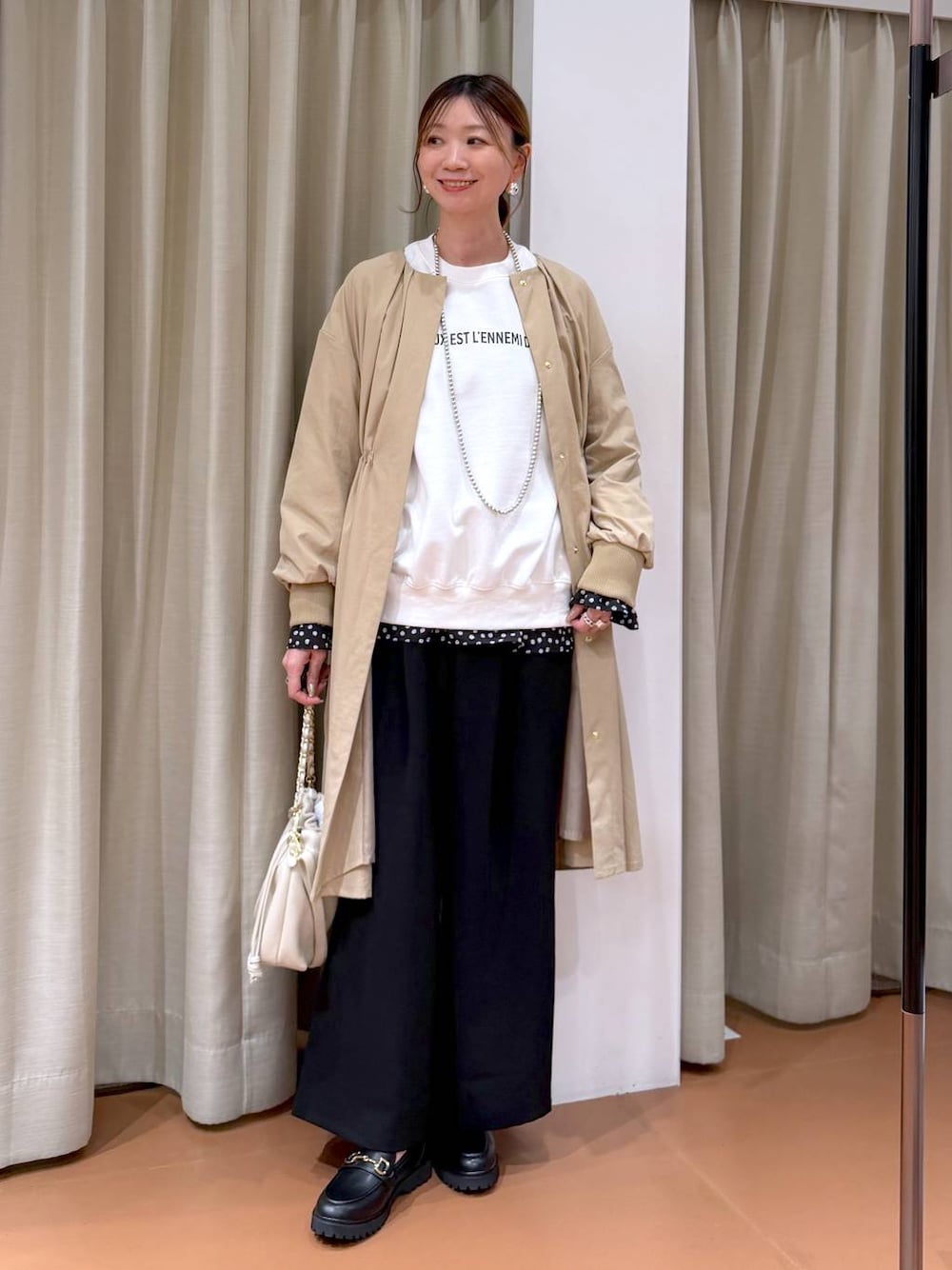 ホワイト系のハンドバッグ、ベージュ系のノーカラーコート、ブラック系のローファーを着用したレディースの冬コーディネートの1枚目の写真