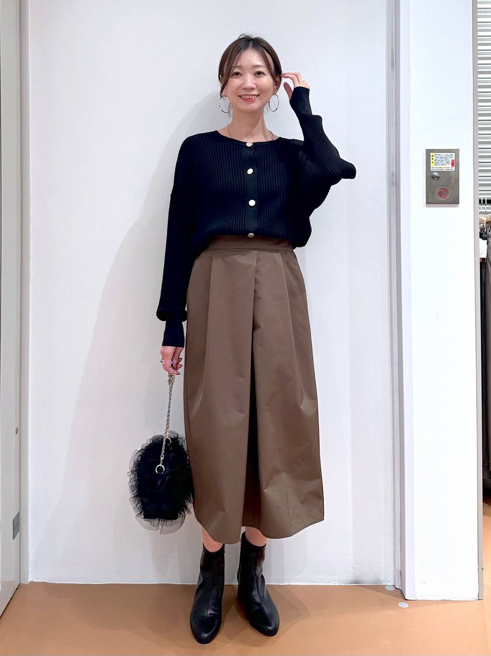ブラック系のカーディガン/ボレロ、ブラウン系のスカート、ブラック系のブーツを着用したレディースの秋コーディネートの1枚目の写真