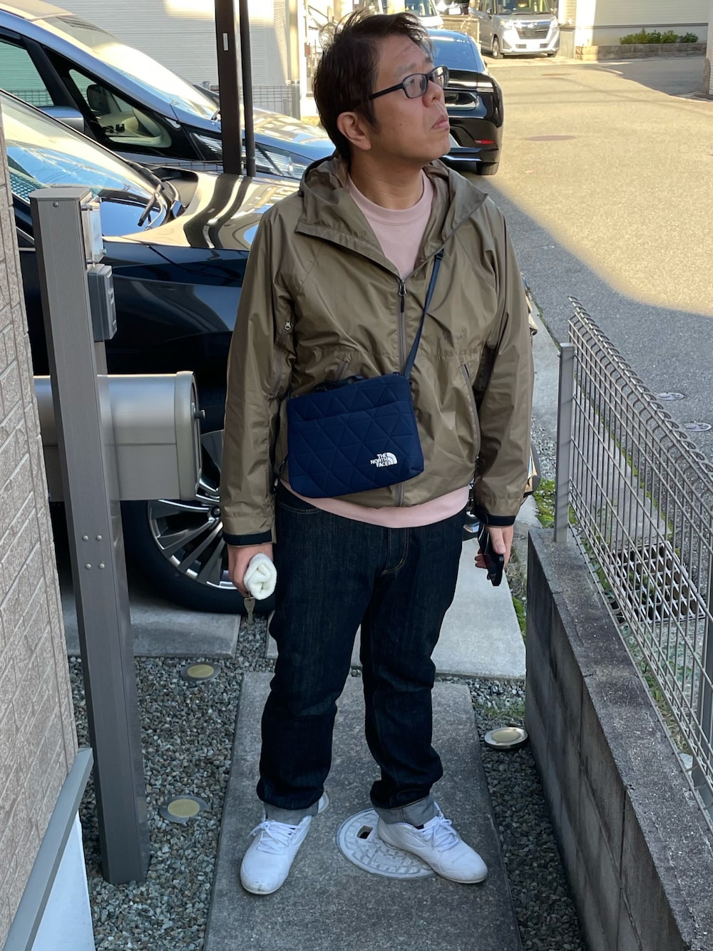 ベージュ系のマウンテンパーカー、ブルー系のショルダーバッグ、ブラック系のデニムパンツを着用したメンズの秋コーディネートの1枚目の写真