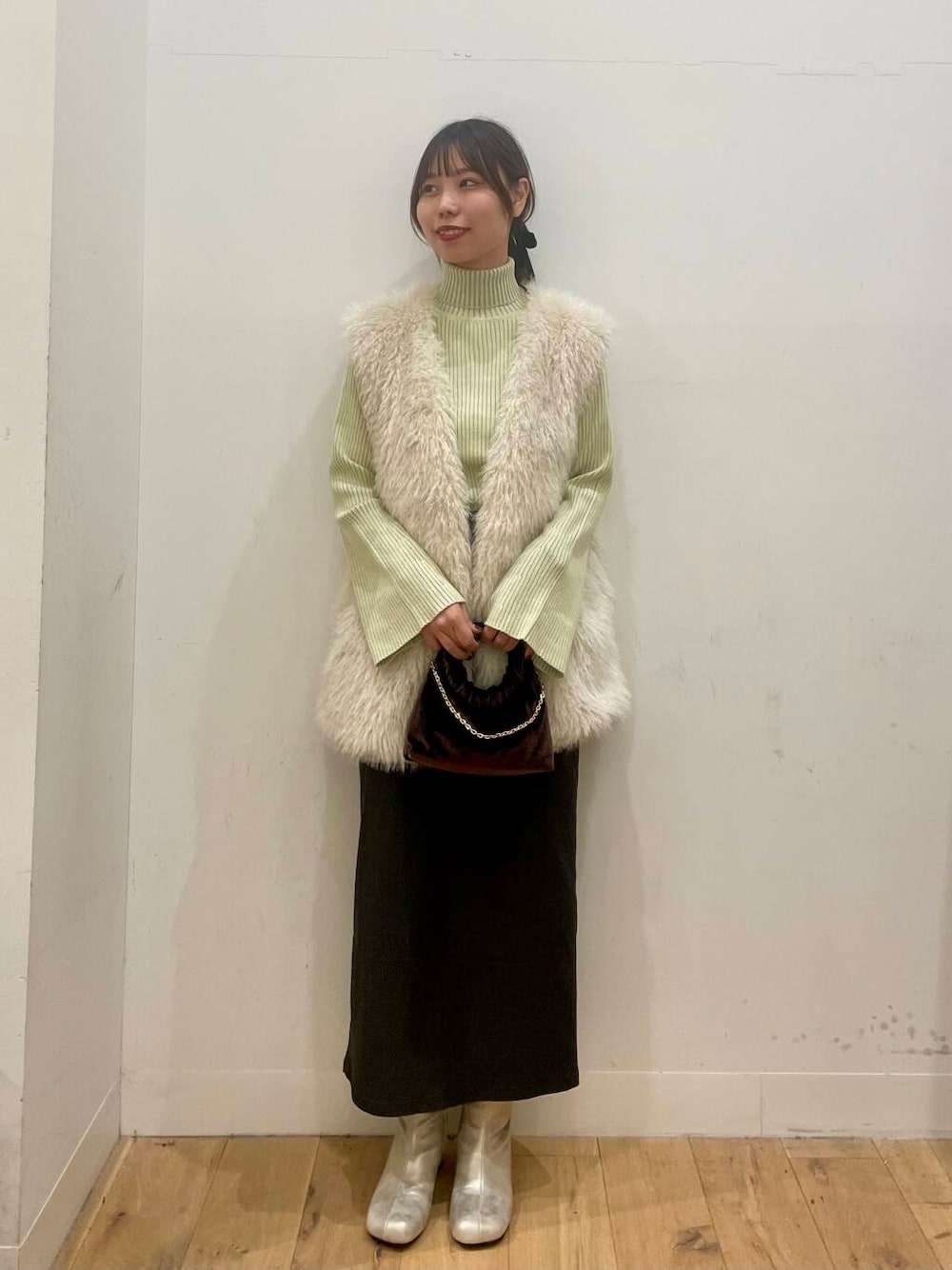 イエロー系のニット/セーター、グレー系のスカート、ブラウン系のハンドバッグを着用したレディースの秋コーディネートの1枚目の写真