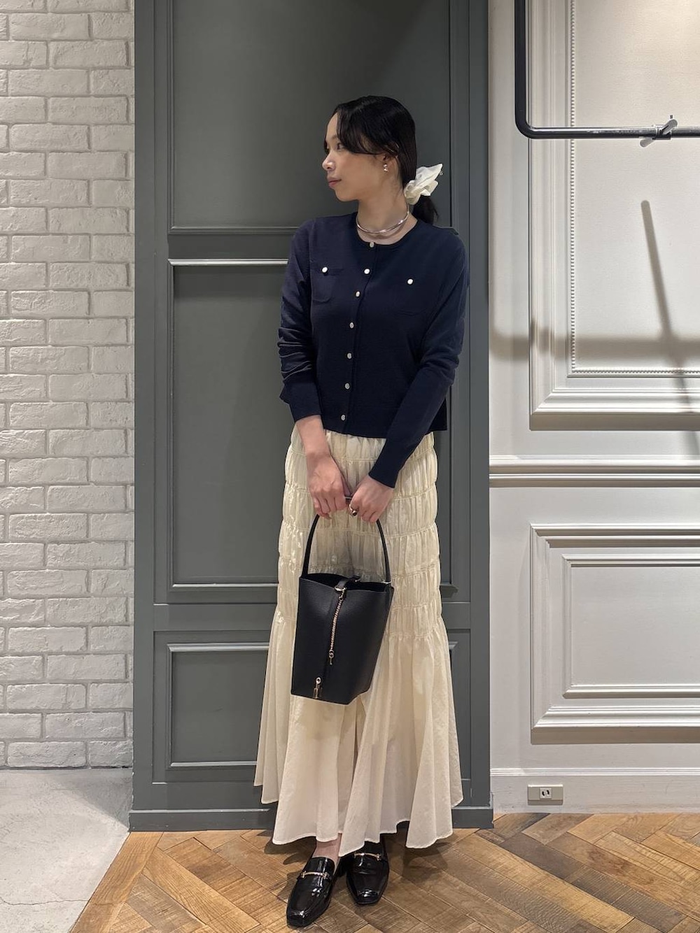 ブラック系のショルダーバッグ、ホワイト系のスカート、ブルー系のカーディガン/ボレロを着用したレディースの冬コーディネートの1枚目の写真