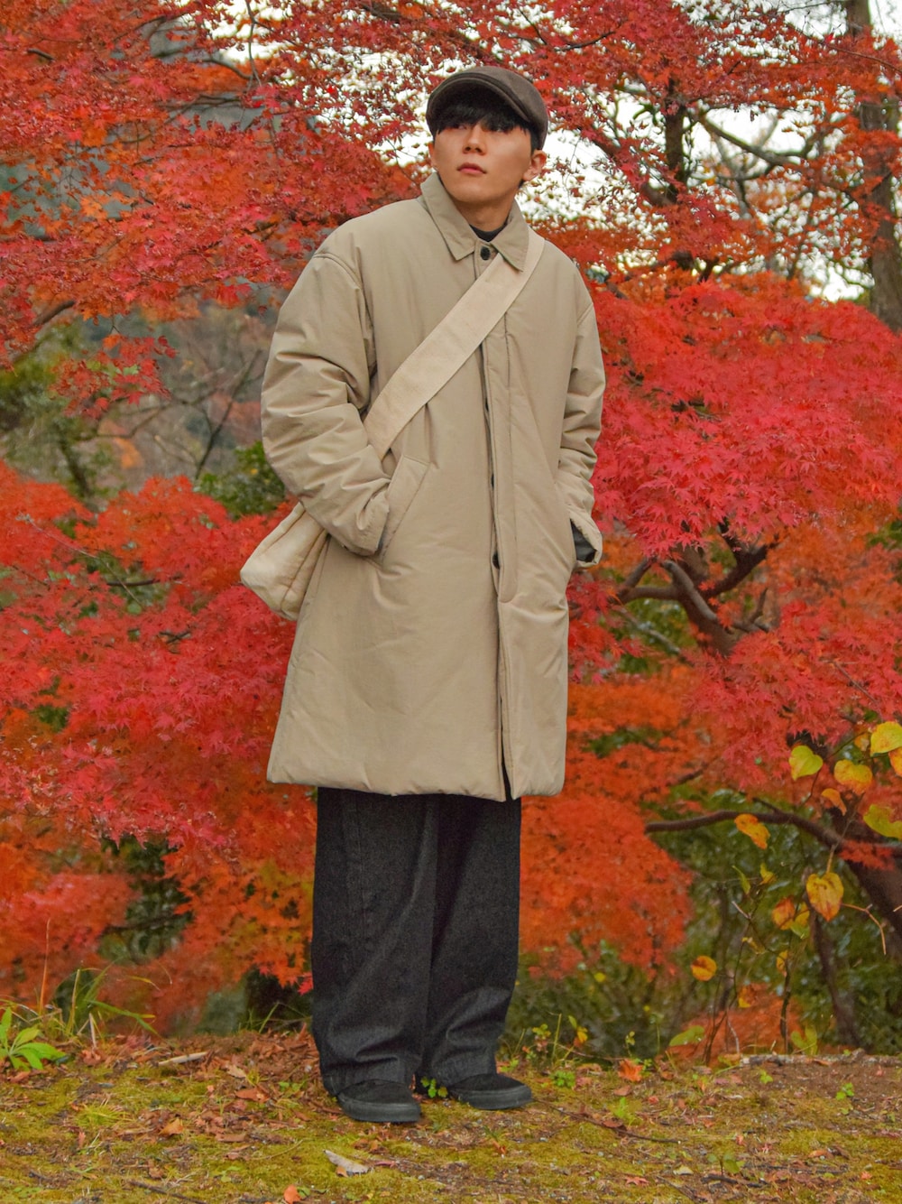 ベージュ系のステンカラーコート、ブラック系のデニムパンツ、ブラック系のスニーカーを着用したメンズの冬コーディネートの1枚目の写真