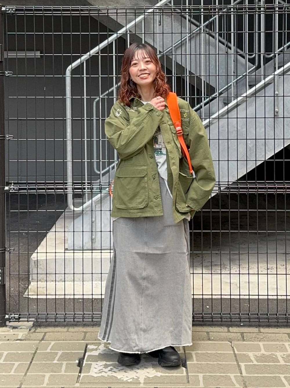 グリーン系のシャツ/ブラウス、オレンジ系のバックパック/リュック、ホワイト系のTシャツ/カットソーを着用したレディースの春コーディネートの1枚目の写真