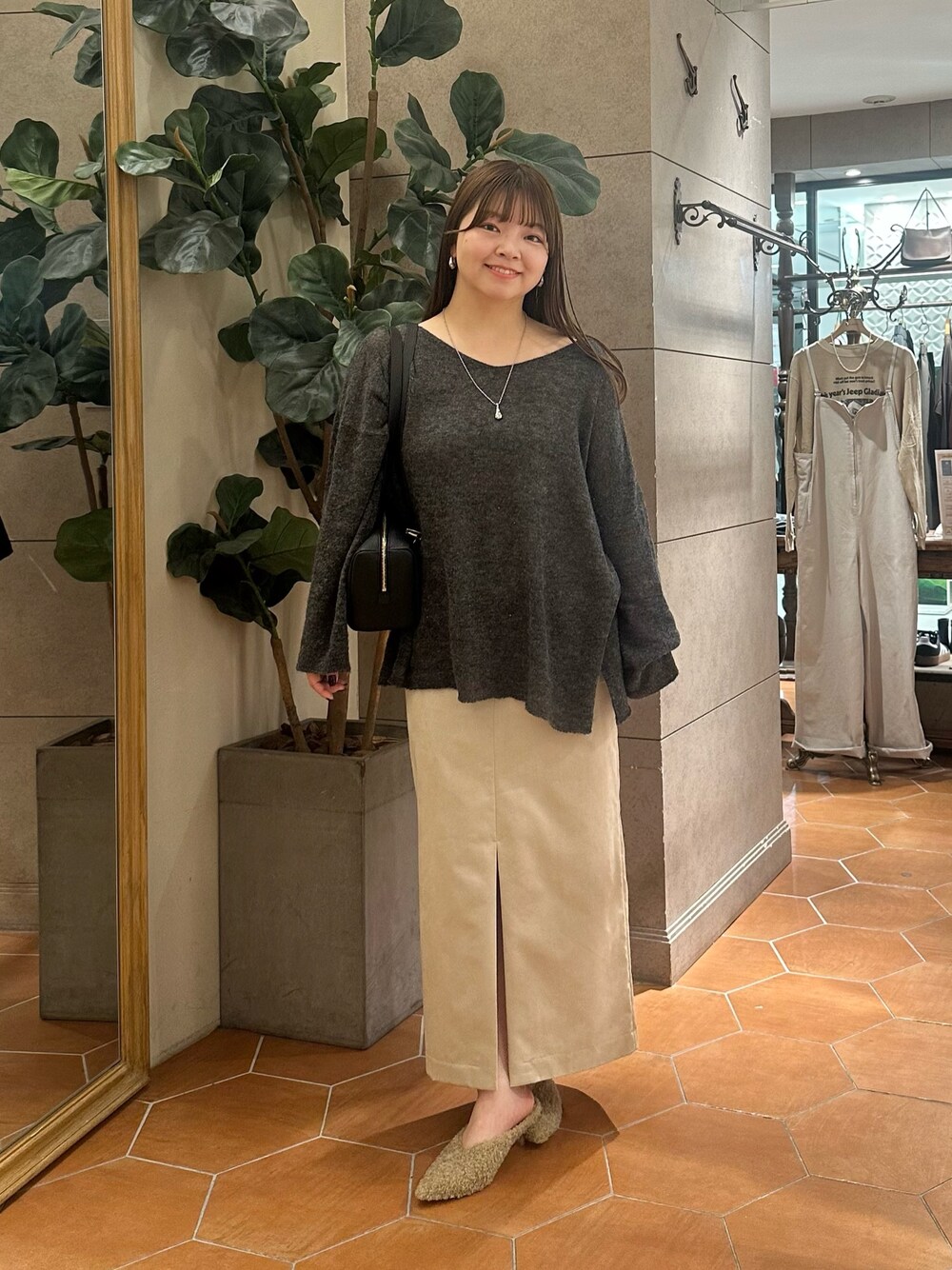 グレー系のニット/セーター、ベージュ系のスカート、ブラック系のショルダーバッグを着用したレディースの秋コーディネートの1枚目の写真