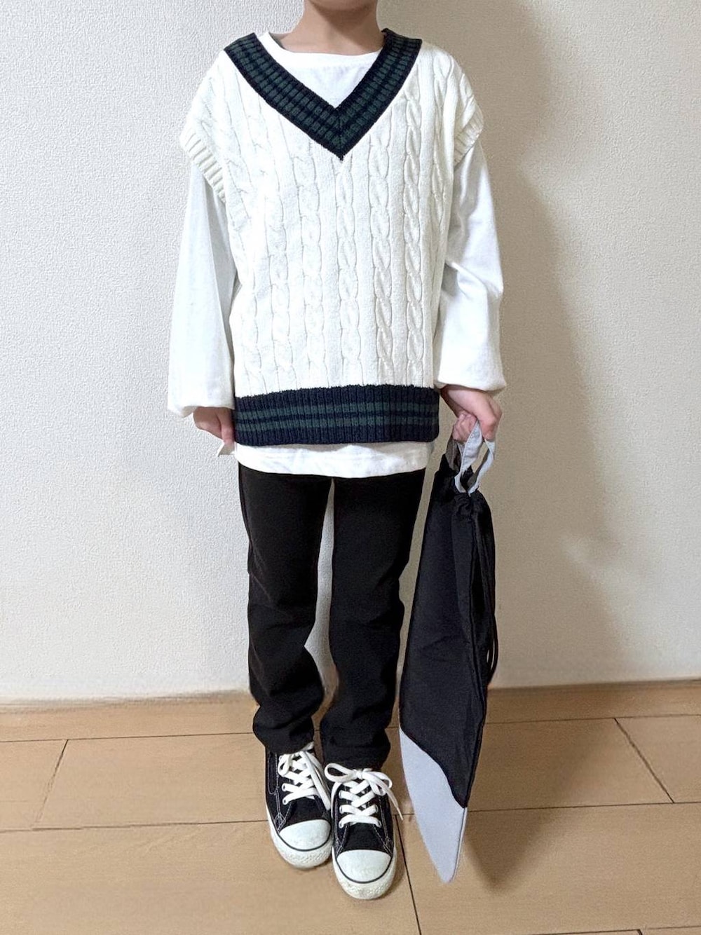 ブラック系のデニムパンツ、ベージュ系のベスト、ブラック系のハンドバッグを着用したキッズの冬コーディネートの1枚目の写真