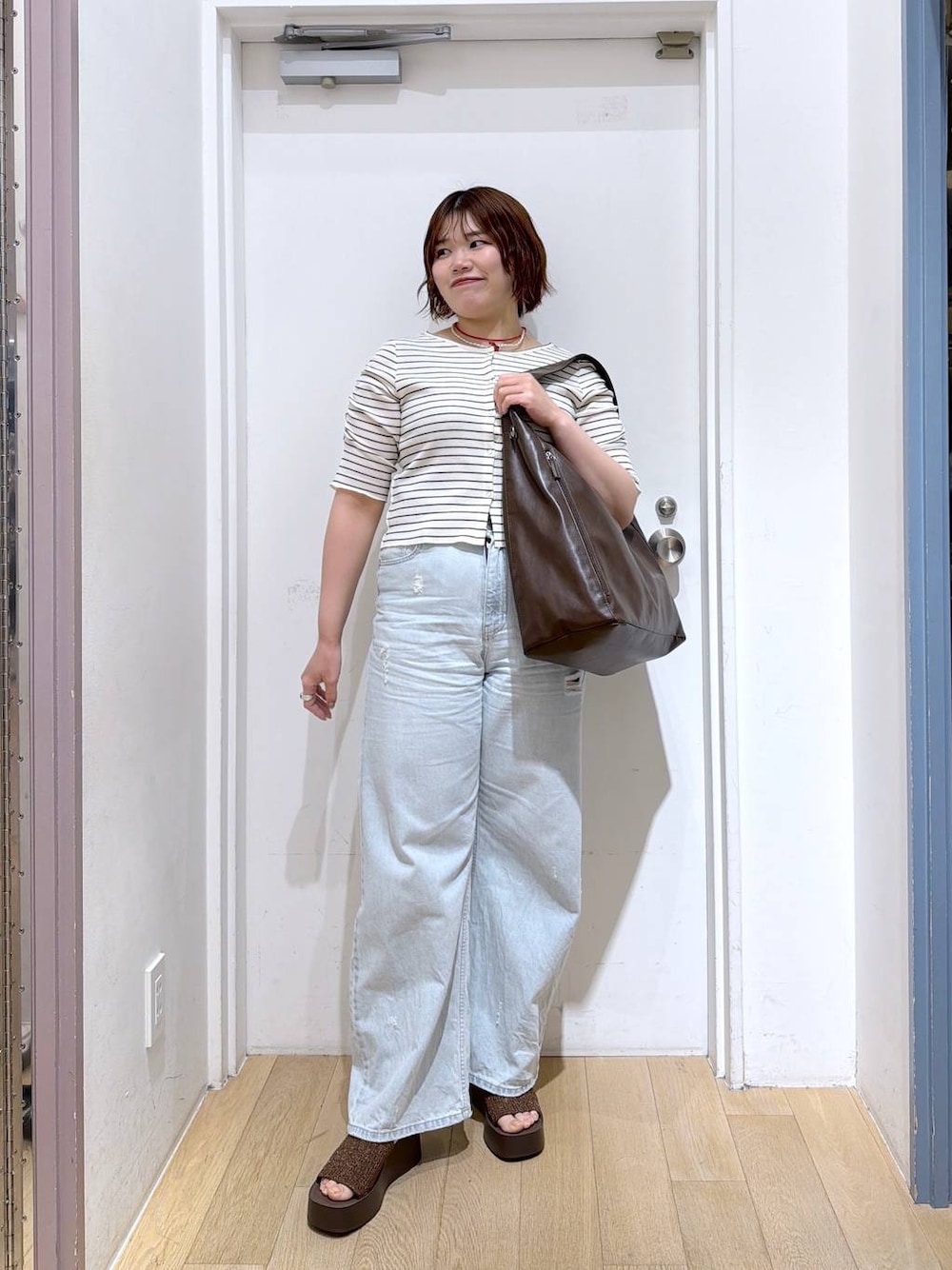 ブルー系のデニムパンツ、ブラウン系のショルダーバッグ、ブラウン系のサンダルを着用したレディースの春コーディネートの1枚目の写真