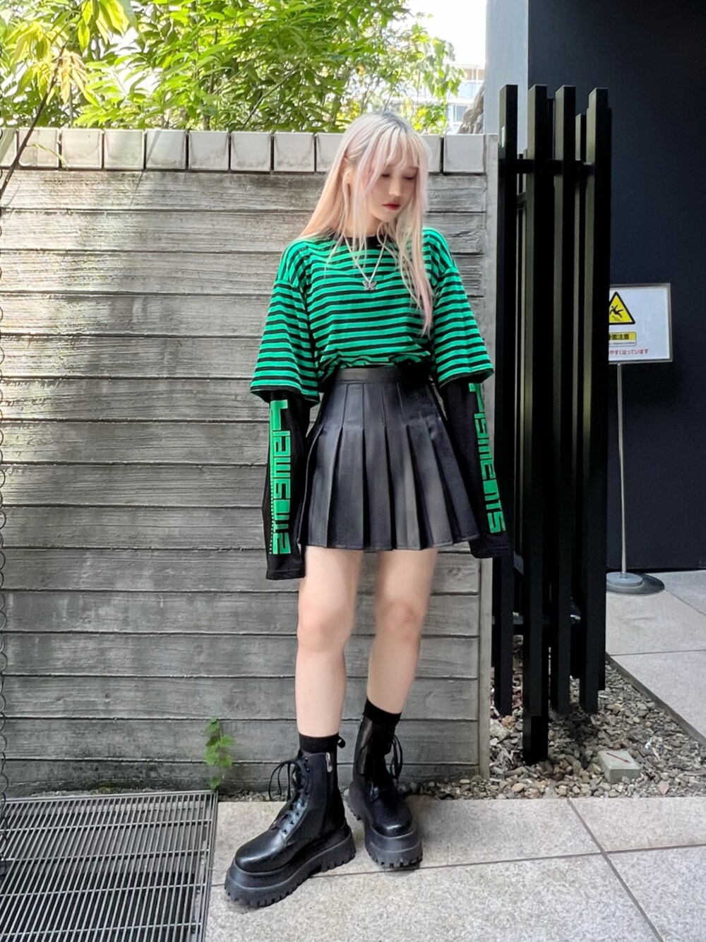 ブラック系のスカート、グリーン系のTシャツ/カットソー、ブラック系のブーツを着用したレディースの秋コーディネートの1枚目の写真