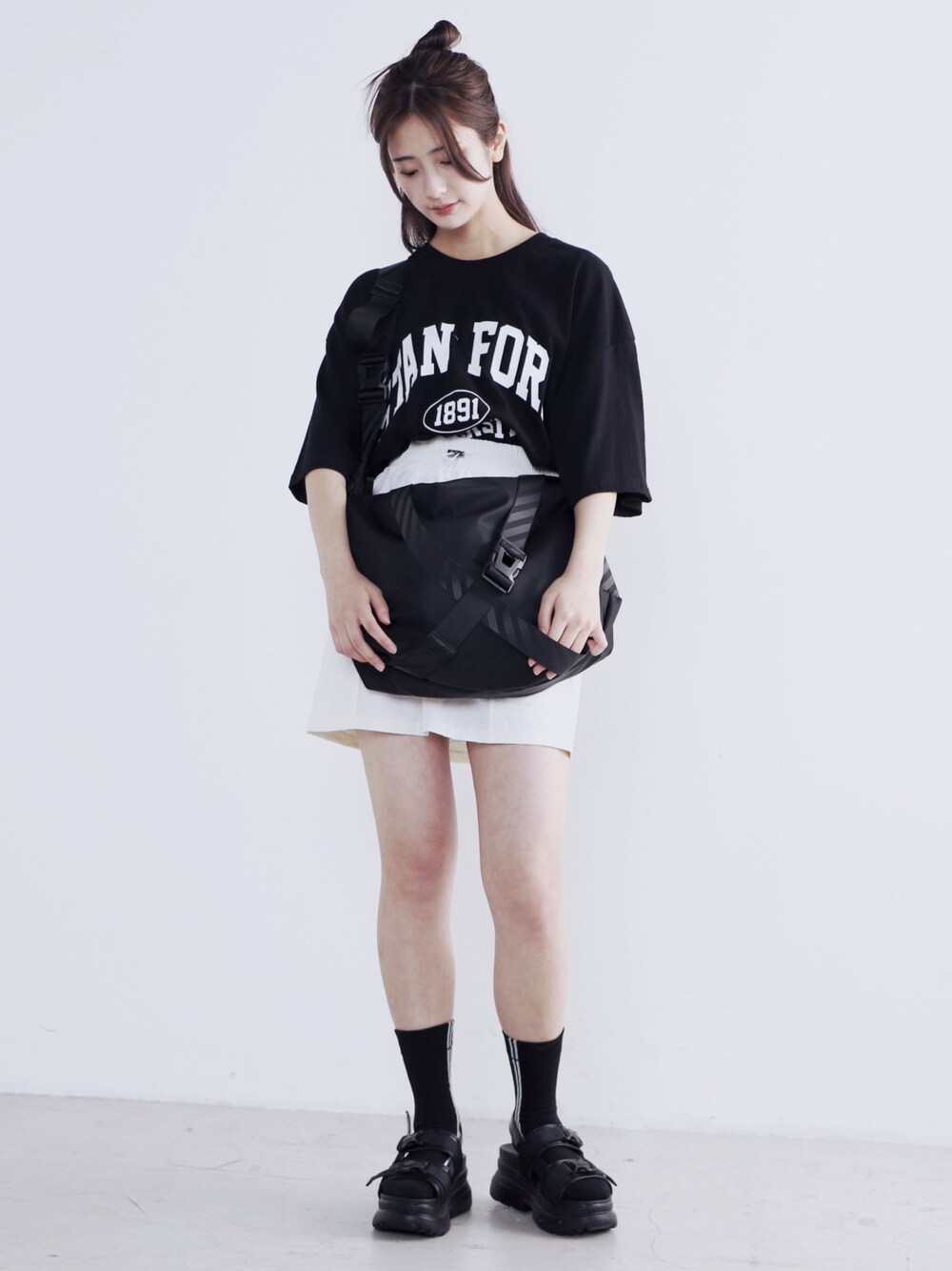ブラック系のショルダーバッグ、ブラック系のTシャツ/カットソー、ホワイト系のスカートを着用したレディースの夏コーディネートの1枚目の写真