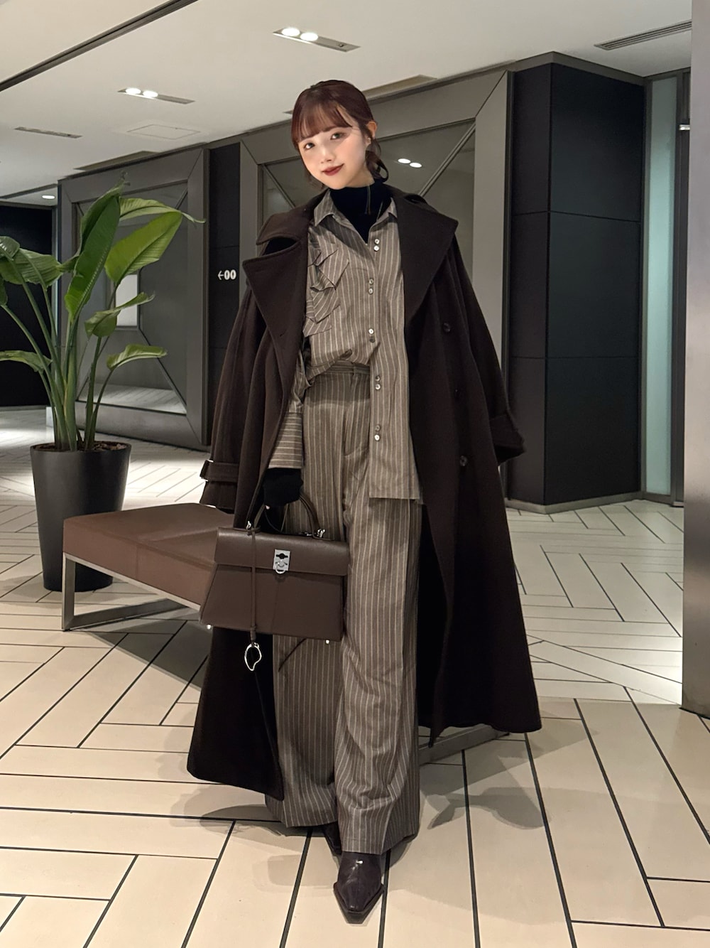 ブラウン系のトレンチコート、ブラウン系のシャツ/ブラウス、ブラック系のニット/セーターを着用したレディースの冬コーディネートの1枚目の写真