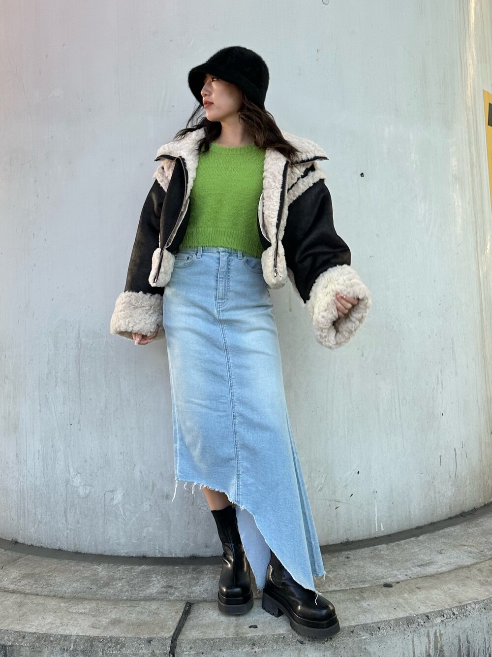 ブルー系のデニムスカート、グリーン系のニット/セーター、ブラック系のムートンコートを着用したレディースの冬コーディネートの1枚目の写真