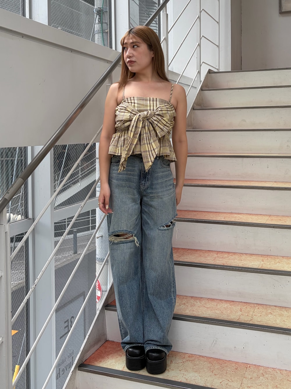イエロー系のキャミソール、ブルー系のデニムパンツ、ブラック系のブーツを着用したレディースの夏コーディネートの1枚目の写真