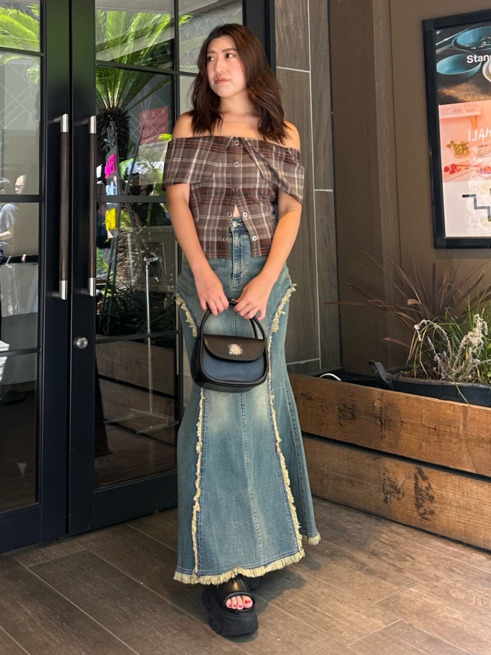 ブラック系のハンドバッグ、ブラック系のサンダル、ブルー系のデニムスカートを着用したレディースの夏コーディネートの1枚目の写真