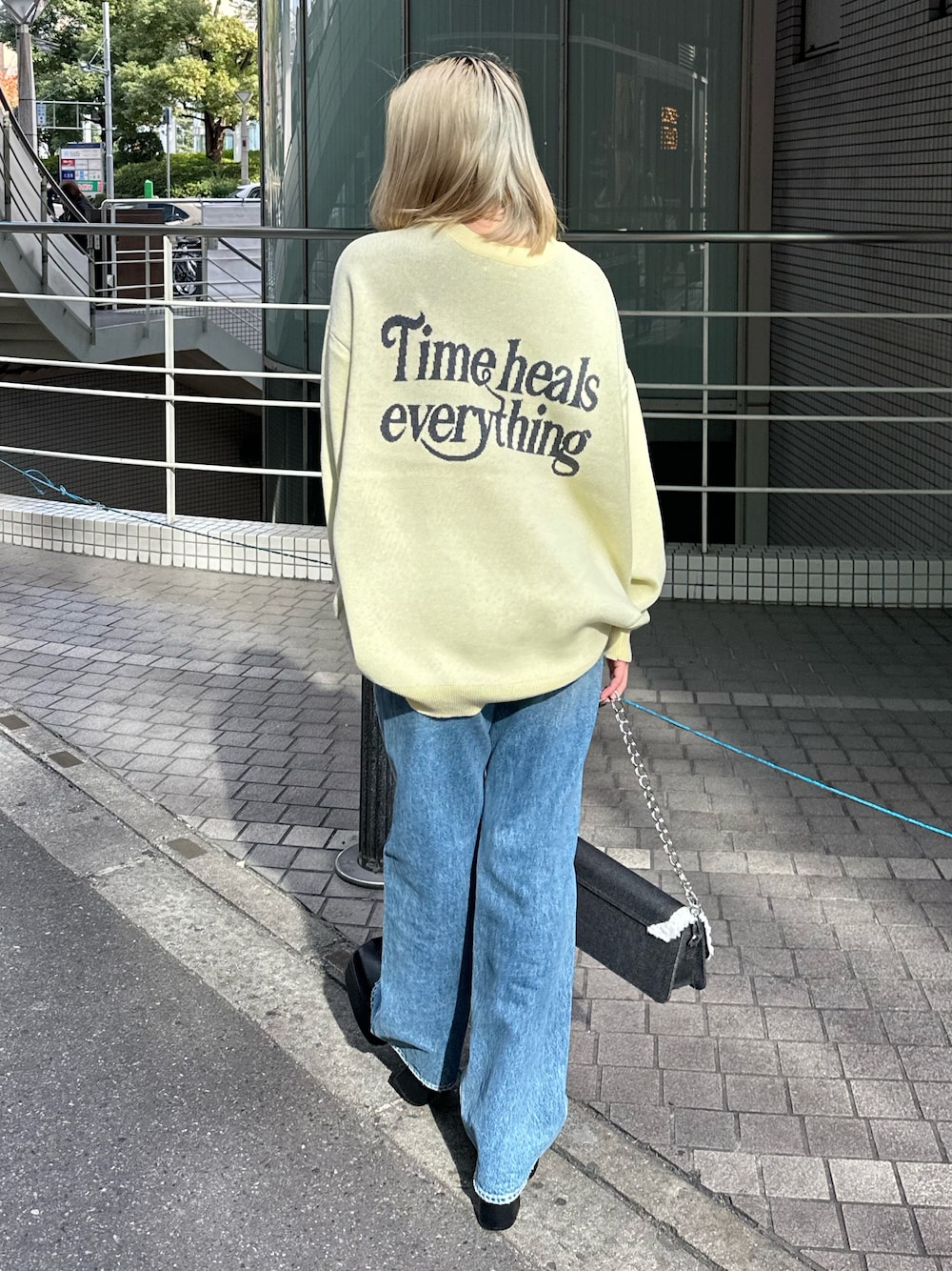 イエロー系のニット/セーター、ブルー系のデニムパンツ、ブラック系のショルダーバッグを着用したレディースの冬コーディネートの1枚目の写真