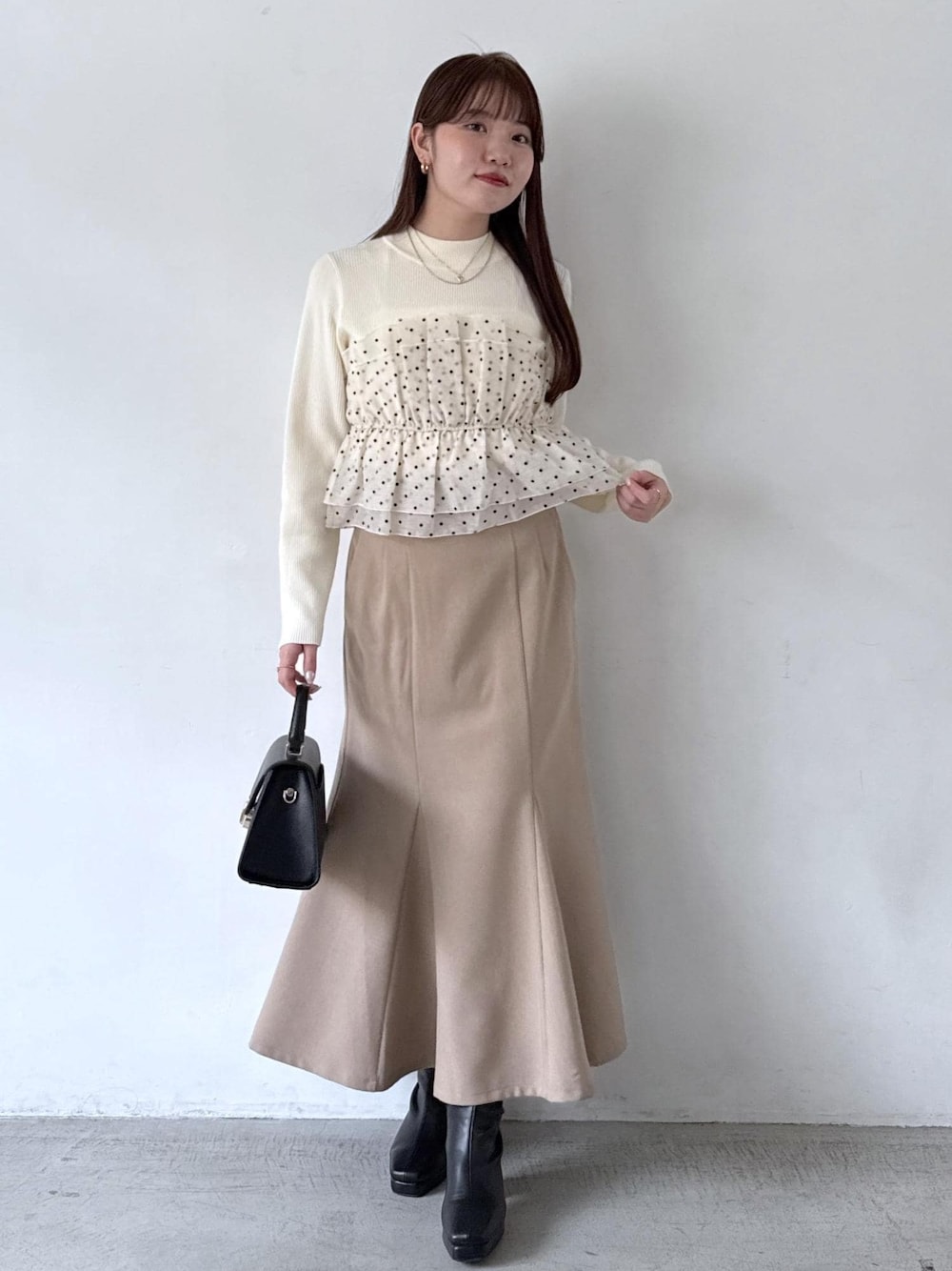 ホワイト系のキャミソール、ベージュ系のスカート、ブラック系のブーツを着用したレディースの秋コーディネートの1枚目の写真