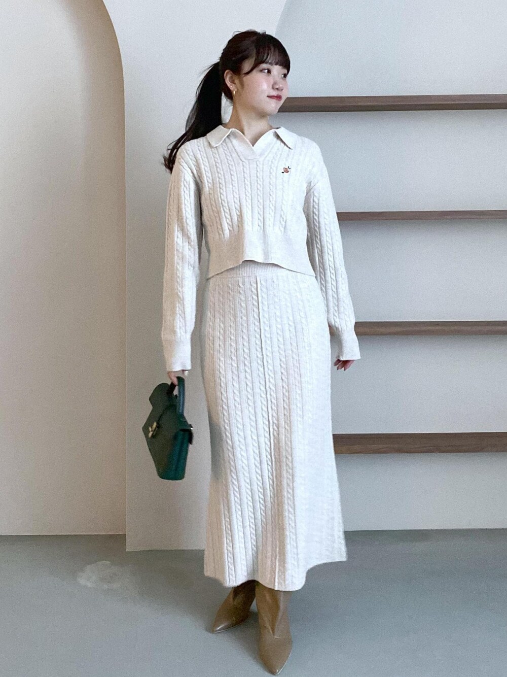 グリーン系のショルダーバッグ、ベージュ系のブーツ、ベージュ系のスカートを着用したレディースの冬コーディネートの1枚目の写真