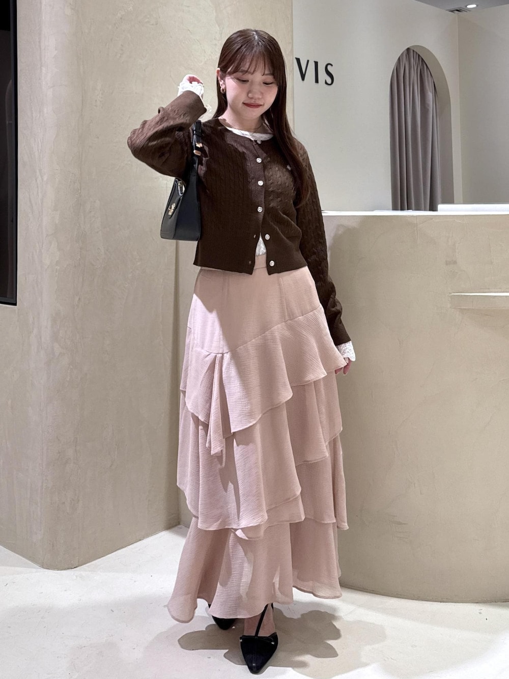 ブラック系のパンプス、ピンク系のスカート、ブラウン系のカーディガン/ボレロを着用したレディースの秋コーディネートの1枚目の写真