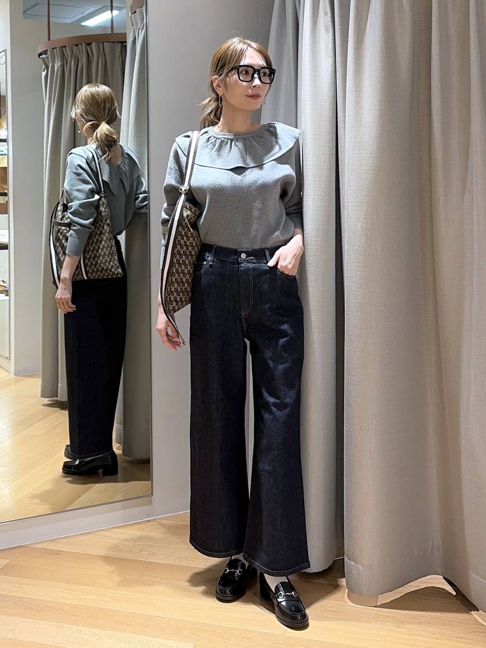 ブルー系のデニムパンツ、ブラウン系のショルダーバッグ、グレー系のニット/セーターを着用したレディースの冬コーディネートの1枚目の写真