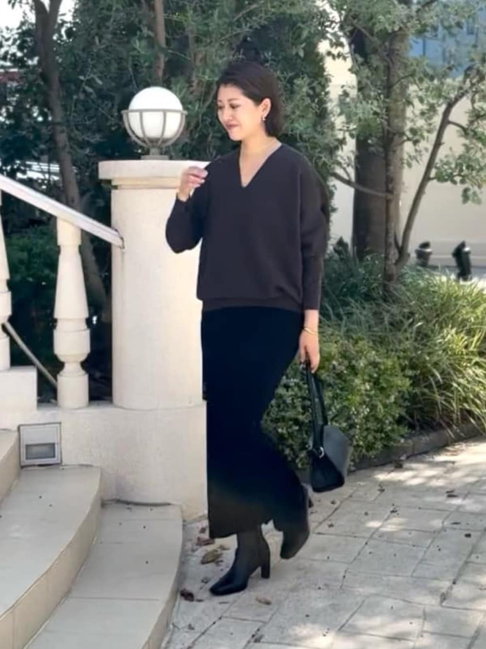 グレー系のニット/セーター、ブラック系のハンドバッグ、ブラック系のスカートを着用したレディースの秋コーディネートの1枚目の写真