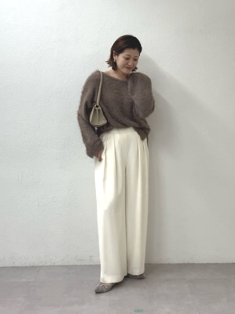 ブラウン系のニット/セーター、ホワイト系のスラックス、ベージュ系のハンドバッグを着用したレディースの秋コーディネートの1枚目の写真