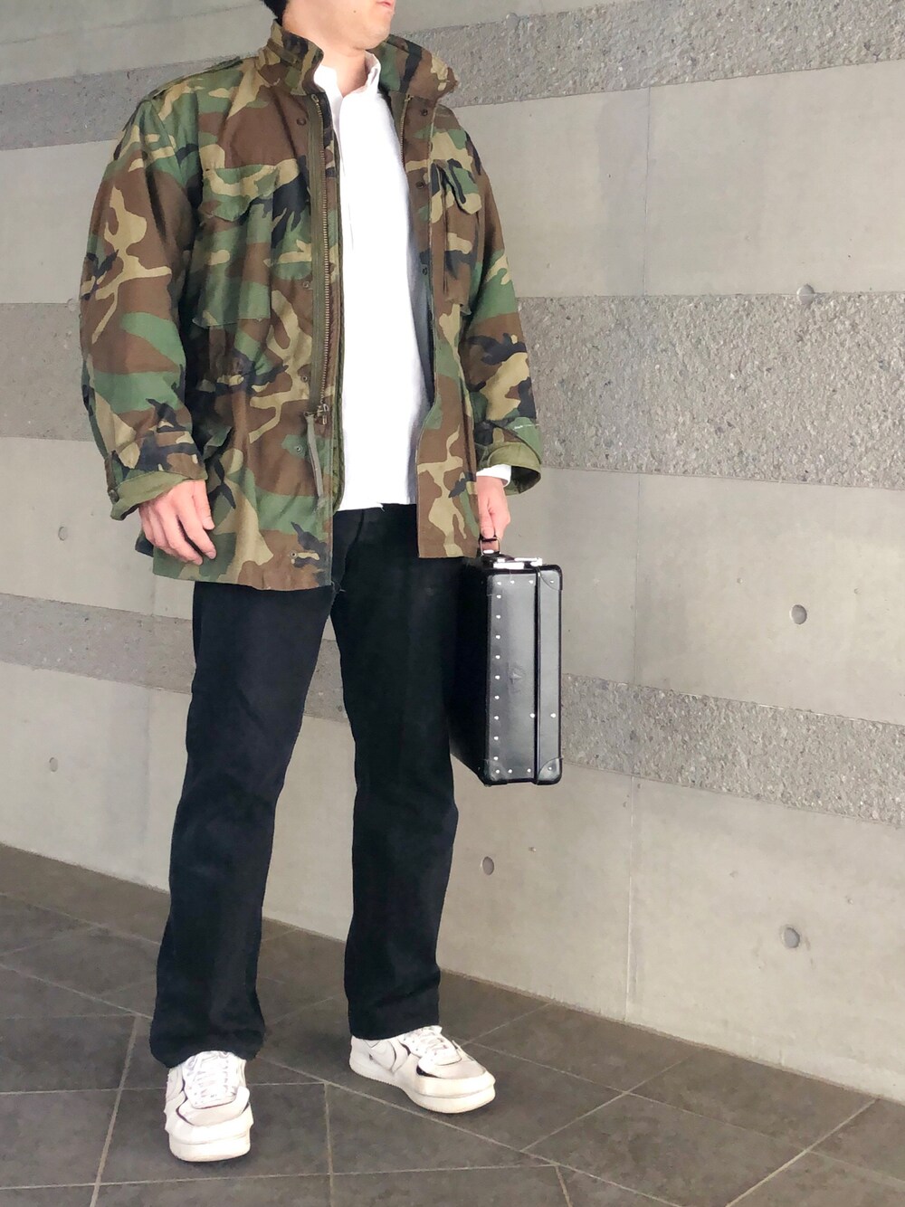 ブラック系のデニムパンツ、ホワイト系のスニーカー、その他のミリタリージャケットを着用したメンズの春コーディネートの1枚目の写真