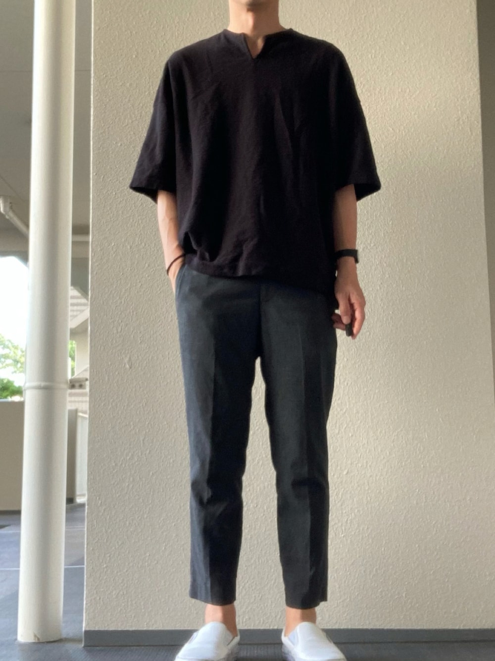 グレー系のスラックス、ブラック系のTシャツ/カットソー、ホワイト系のスリッポンを着用したメンズの夏コーディネートの1枚目の写真