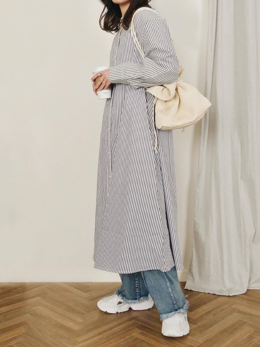 ブラック系のシャツワンピース、ホワイト系のショルダーバッグ、ブルー系のデニムパンツを着用したレディースの冬コーディネートの1枚目の写真