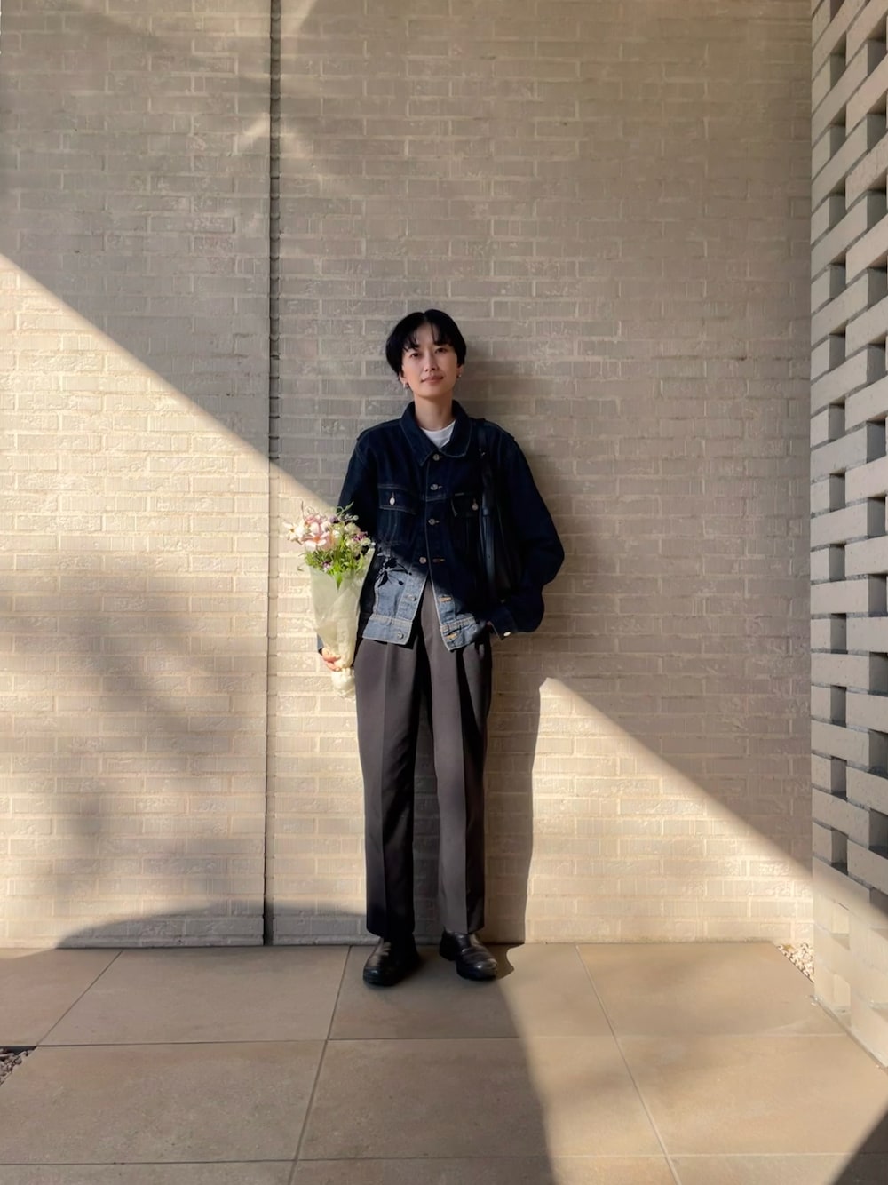 ブラック系のスラックス、ブラック系のブーツを着用したレディースの春コーディネートの1枚目の写真