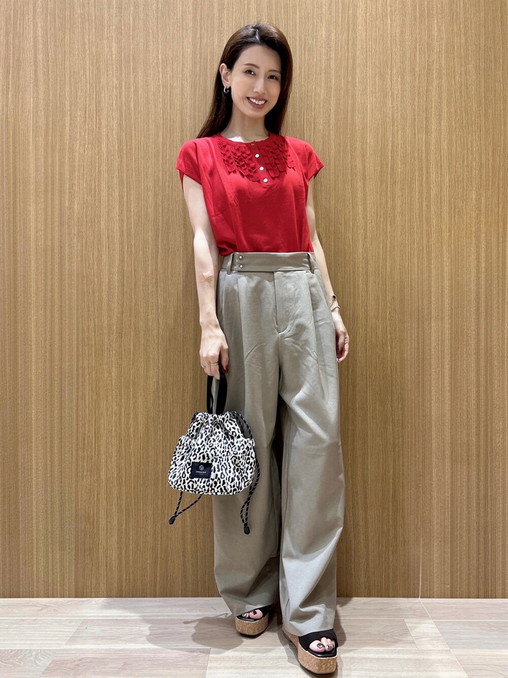 レッド系のニット/セーター、ブラウン系のその他パンツ、ベージュ系のショルダーバッグを着用したレディースの夏コーディネートの1枚目の写真