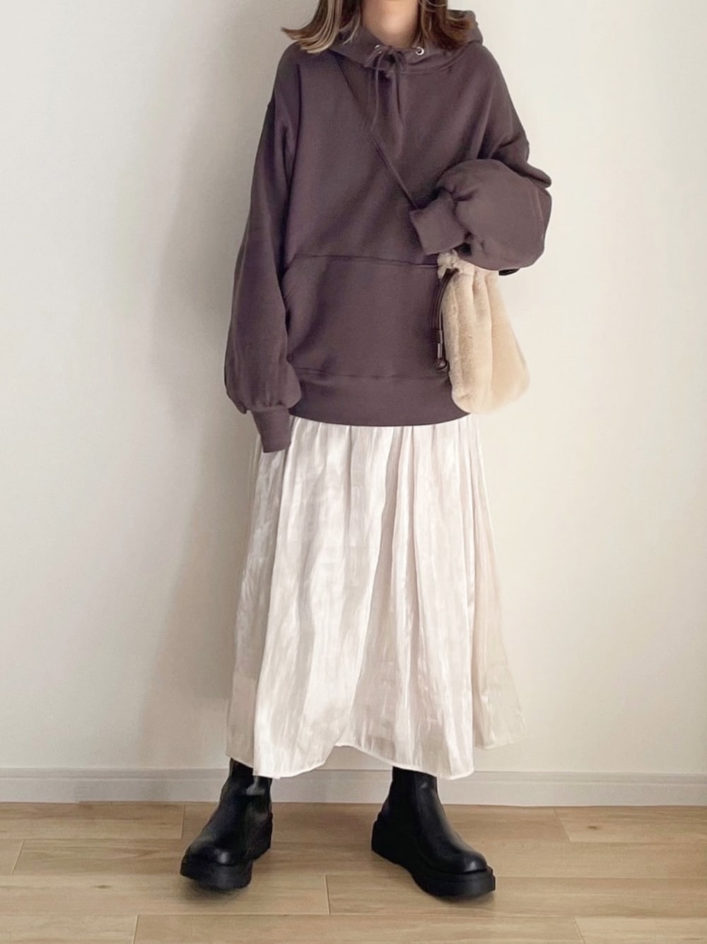 グレー系のパーカー、ホワイト系のスカート、ブラック系のブーツを着用したレディースの冬コーディネートの1枚目の写真