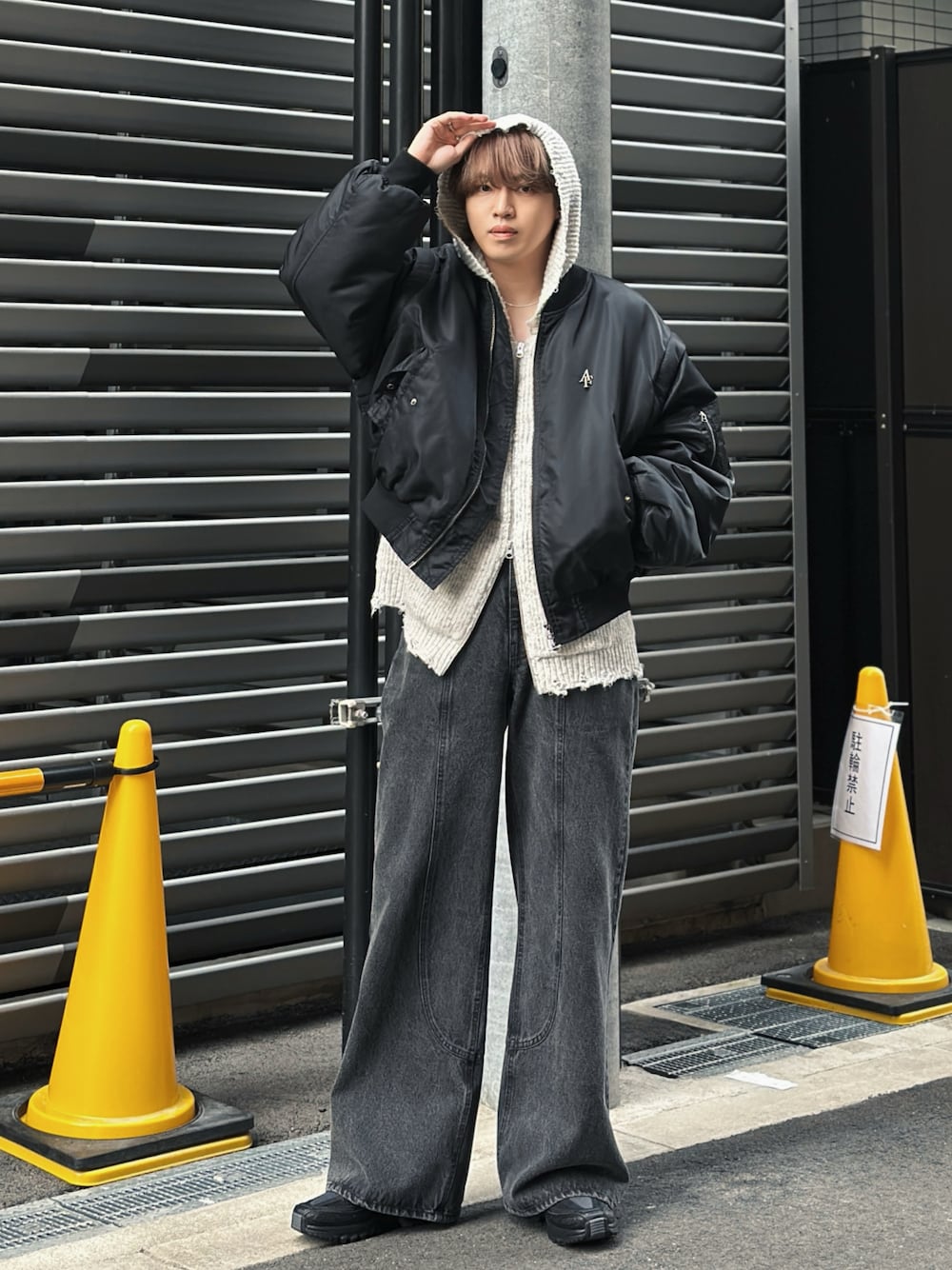Black bomber layered over a grey hoodie with very wide faded dark jeans and dark sneakers